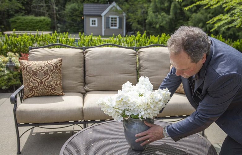 Founding broker of Compass Sam Cunningham adjusts flowers on a patio table in the backyard of a home being listed in Sammamish on Tuesday, May 6, 2025.  230037