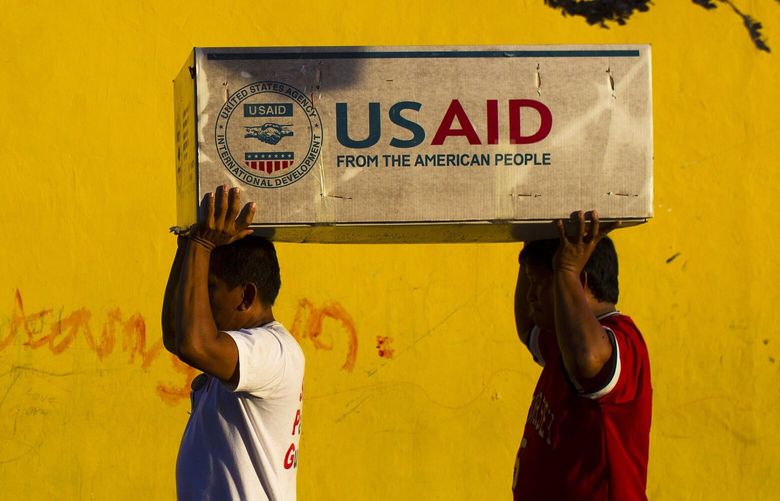 Typhoon Haiyan survivors help carry USAID donated food after a U.S. military helicopter unloaded it in the destroyed town of Guiuan, Philippines on Thursday, Nov. 14, 2013. Aid was beginning to reach some of the half-million people displaced by Typhoon Haiyan that tore across several islands in eastern Philippines six days ago, killing thousands of people.  (AP Photo/David Guttenfelder) XDG104