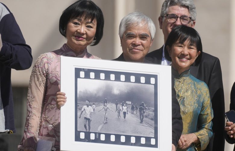 FILE – Pulitzer Prize-winning photographer Nick Ut, center, flanked by Kim Phuc, left, holds the” Napalm Girl”, his Pulitzer Prize winning photo as they wait to meet with Pope Francis during the weekly general audience in St. Peter’s Square at The Vatican, May 11, 2022. (AP Photo/Gregorio Borgia, file) NYPS206 NYPS206