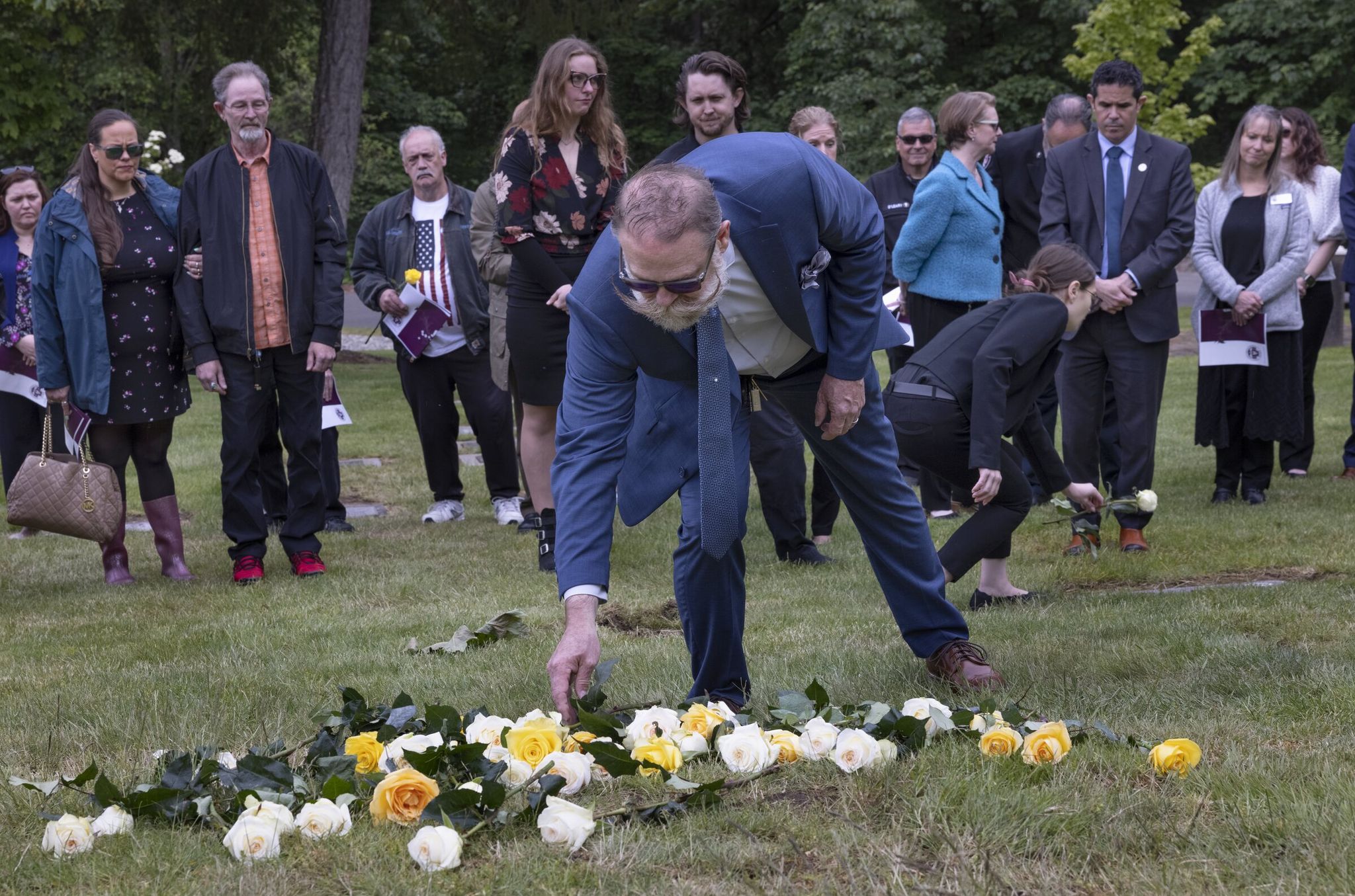 Ron Winter places a rose where 275 urns containing people’s remains were recently buried. At right, Jenna Minichiello, a funeral director at Haven of Rest Funeral Home in Gig Harbor, places a rose on the grave marker where unclaimed bodies were last buried at the funeral home’s cemetery, in 2021. (Ellen M. Banner / The Seattle Times)