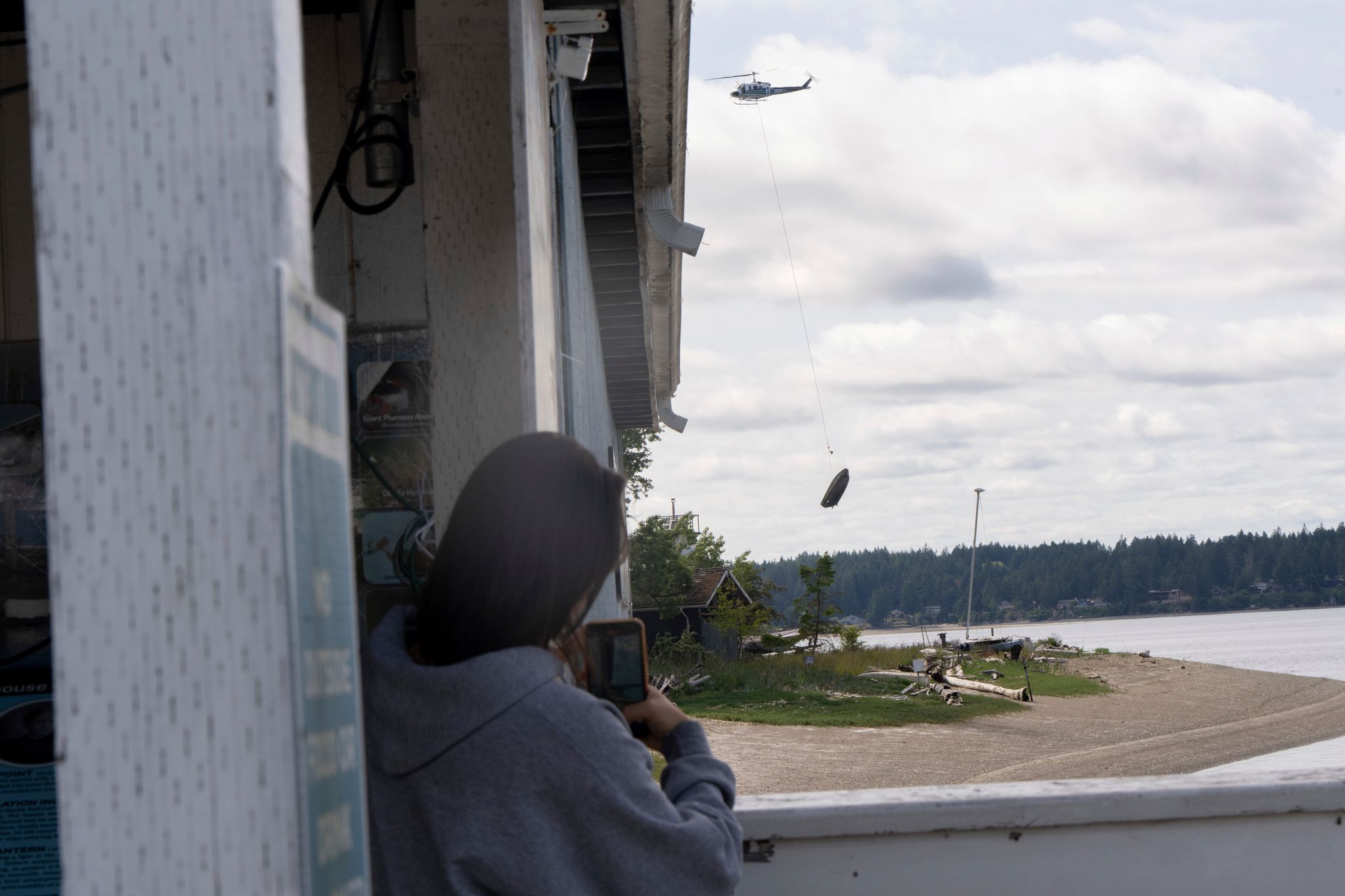 Lucy Trout, from Olympia, watches as an abandoned boat is transported to shore on Wednesday in Olympia. (Jenny Kane / The Associated Press)