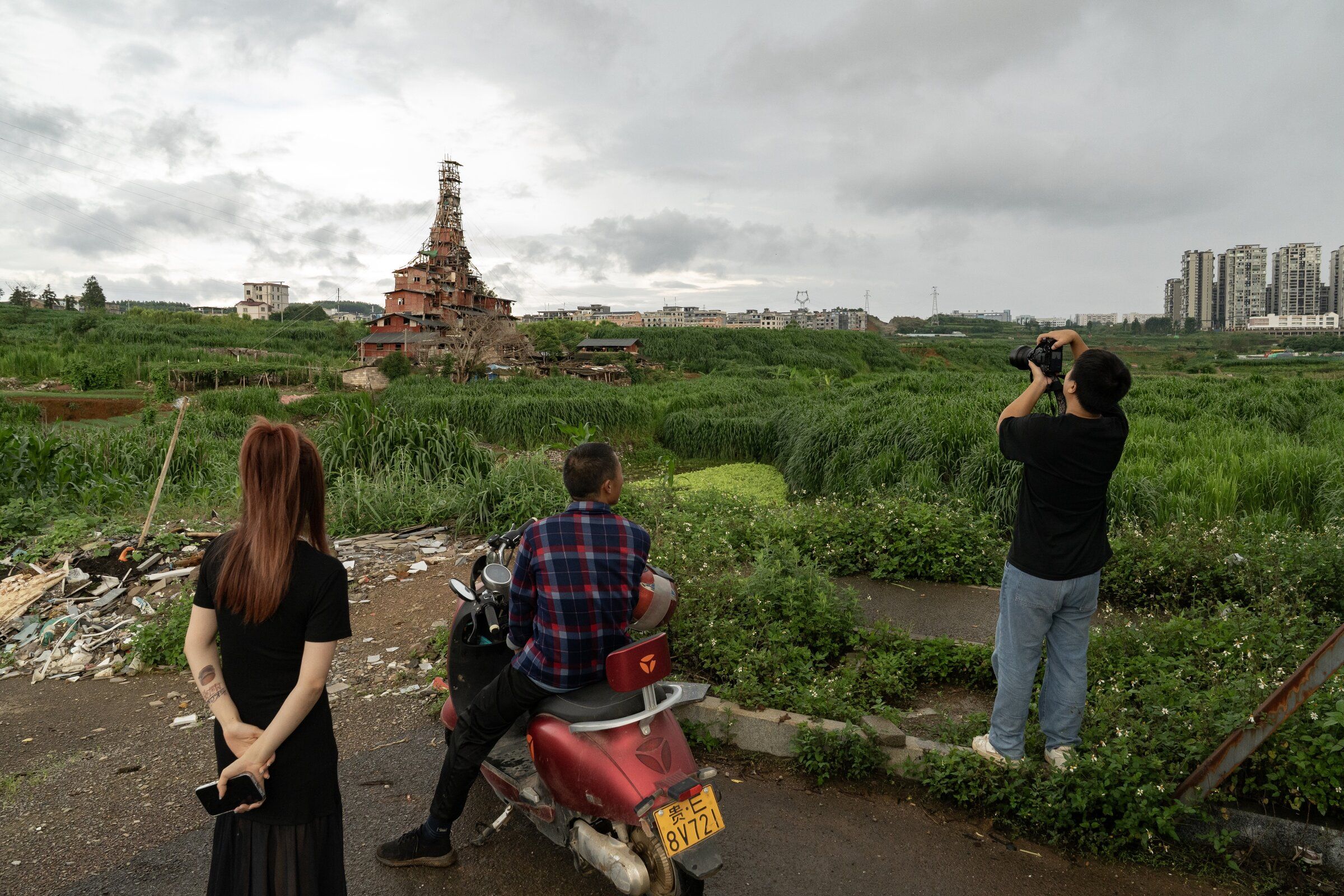 Chen Tianming, on a scooter, chats with people who came to see his rickety multi-story house in Xingyi, China July 1. (Andrea Verdelli / The New York Times)