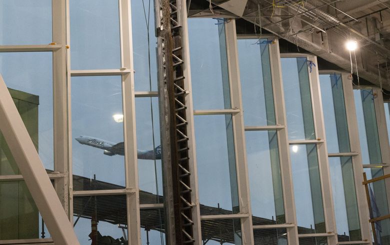 A plane taking off at Sea-Tac can be seen through windows in the airport’s remodeled Concourse C. The space is due to open in the spring. (Ellen M. Banner / The Seattle Times)