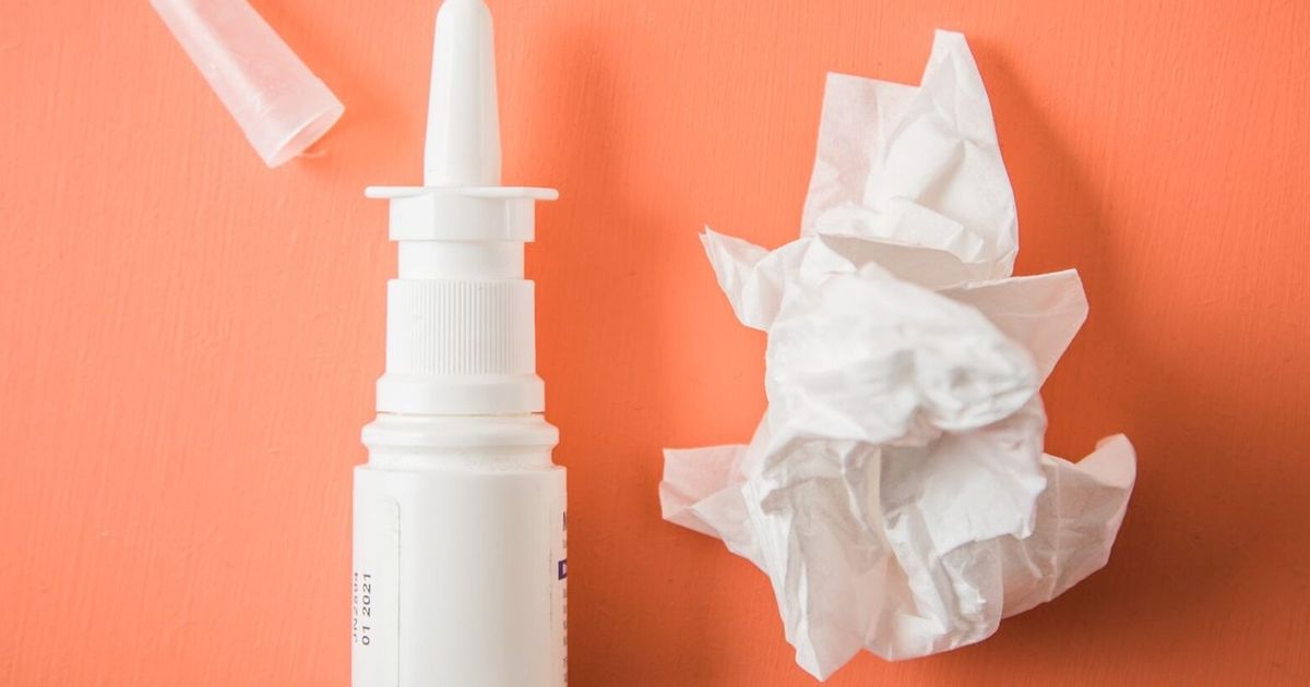 Person holding a decongestant nasal spray bottle near their nose