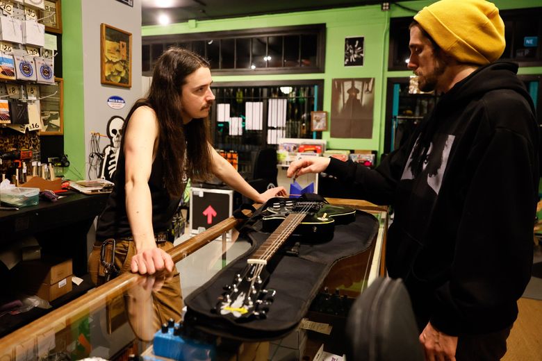 Sam Smallidge, left, chats with Justin Martin as they discuss repair work on Martin’s guitar at Re-Animated Music. (Jennifer Buchanan / The Seattle Times)