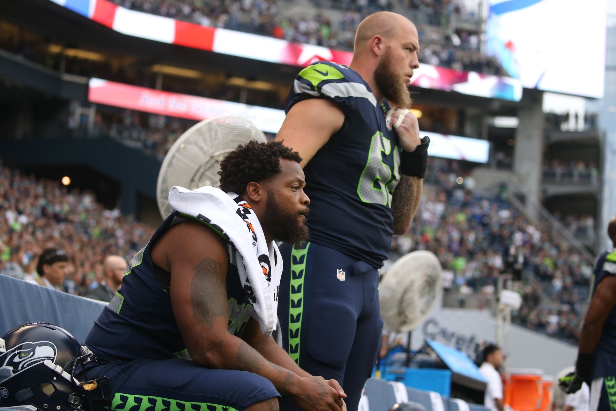 Michael Bennett sits during the national anthem while Justin Britt stands with a hand on Bennett's shoulder before a preseason home game against the Minnesota Vikings on Aug. 18, 2017. (Bettina Hansen / The Seattle Times, 2017)