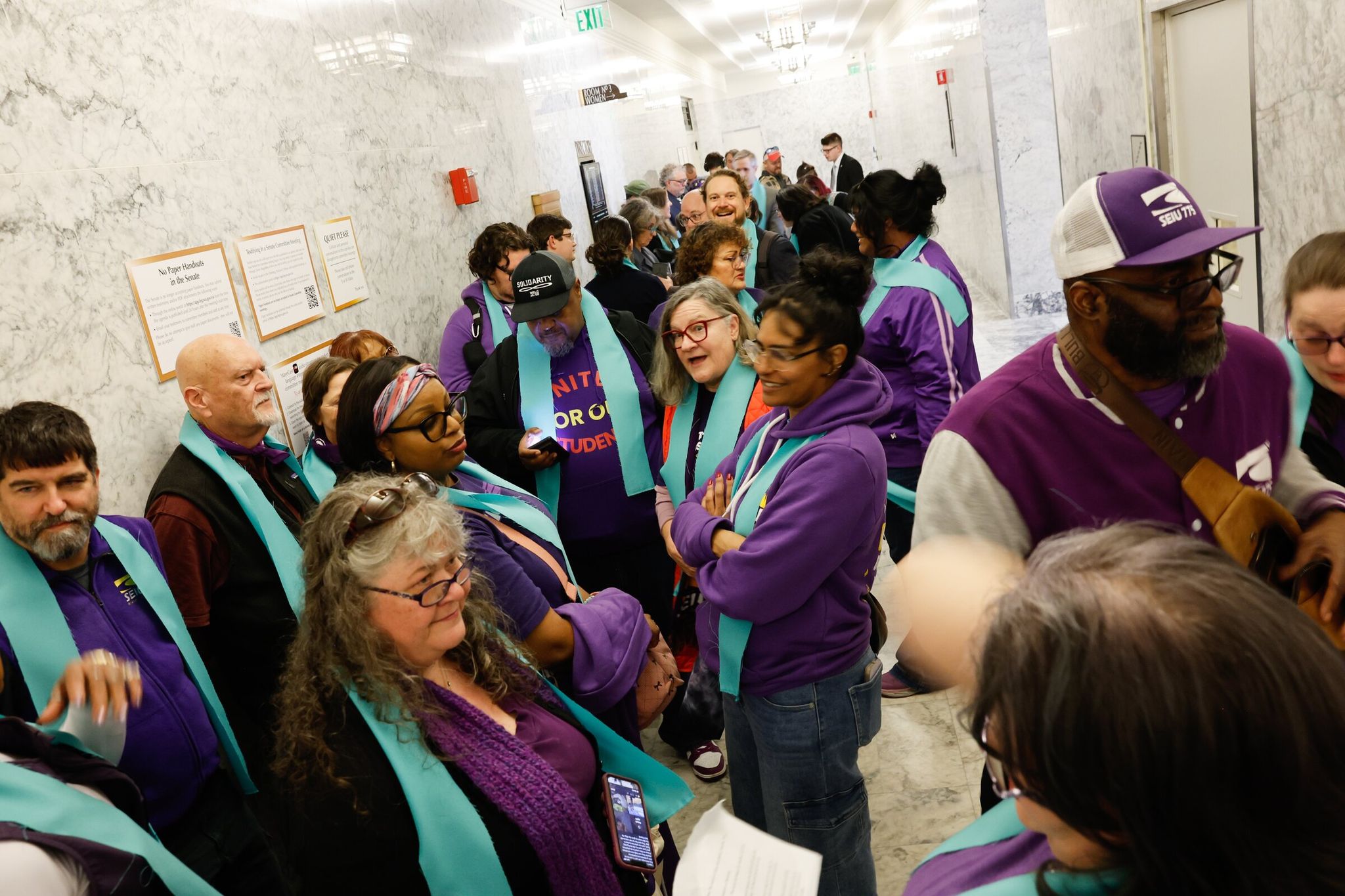 Sara Hartson of Shelton and other supporters of the proposed 'millionaires tax' — all wearing blue scarves — wait at the entrance to the hearing room for the start of the first public hearing on the matter. 'We want to show residents of this state that we need a better tax system — fairer and so that the rich pay their share,' Hartson said. (Karen Ducey / The Seattle Times)