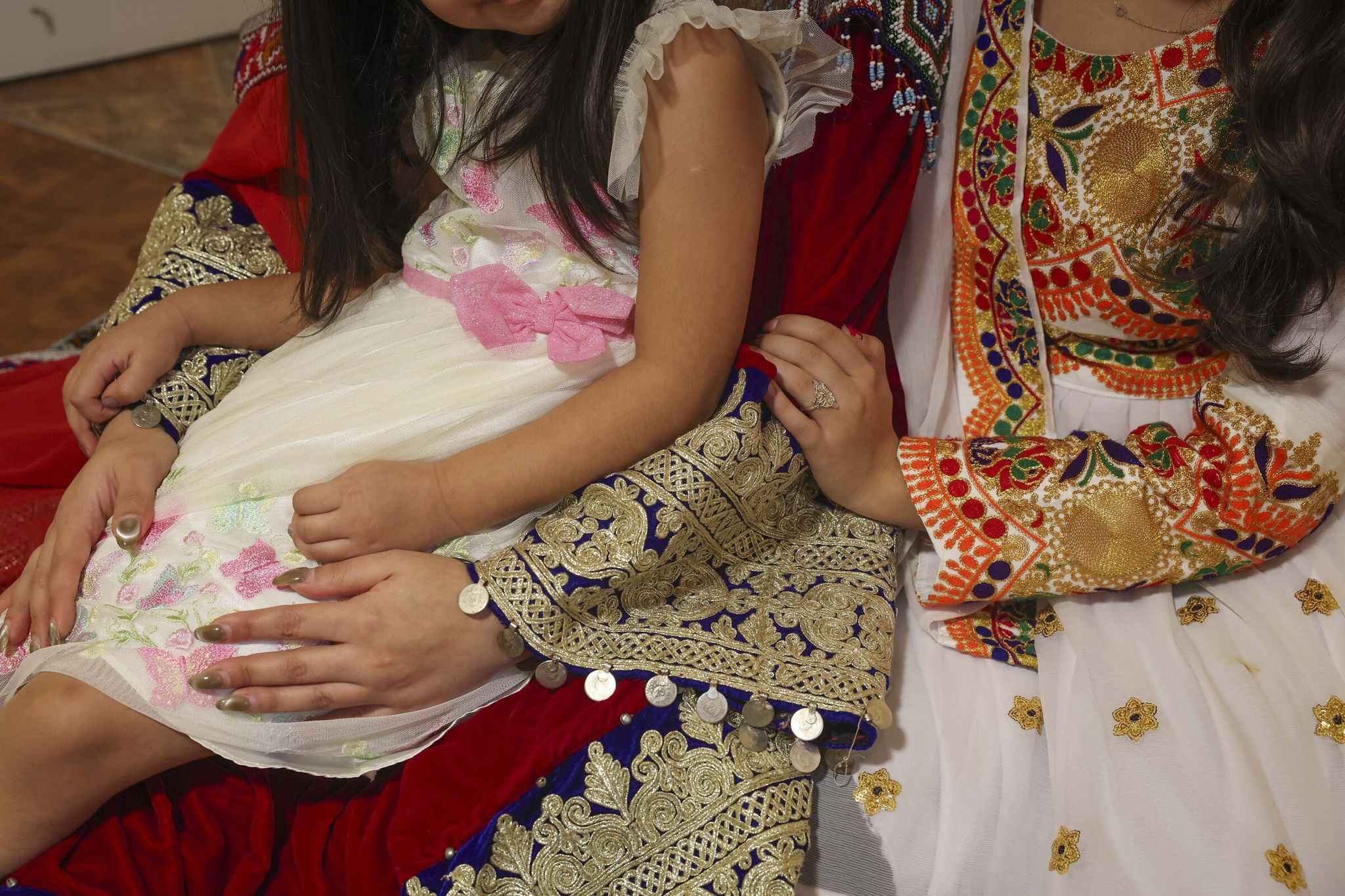 Pari, wearing a red traditional Afghan dress, and her daughters, one also in traditional dress, sit in their Seattle apartment last month. 'For me as a woman it completely changed my life,' she said about moving to the U.S. (Ivy Ceballo / The Seattle Times)