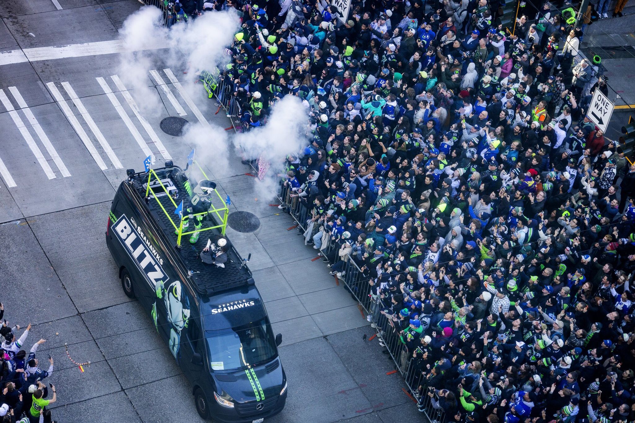 A crowd of Seahawks fans along Fourth Avenue at Madison Street cheers as the team's mascot Blitz passes by on his vehicle, which emits smoke plumes, during the Super Bowl LX victory parade Wednesday in Seattle. (Ken Lambert / The Seattle Times)