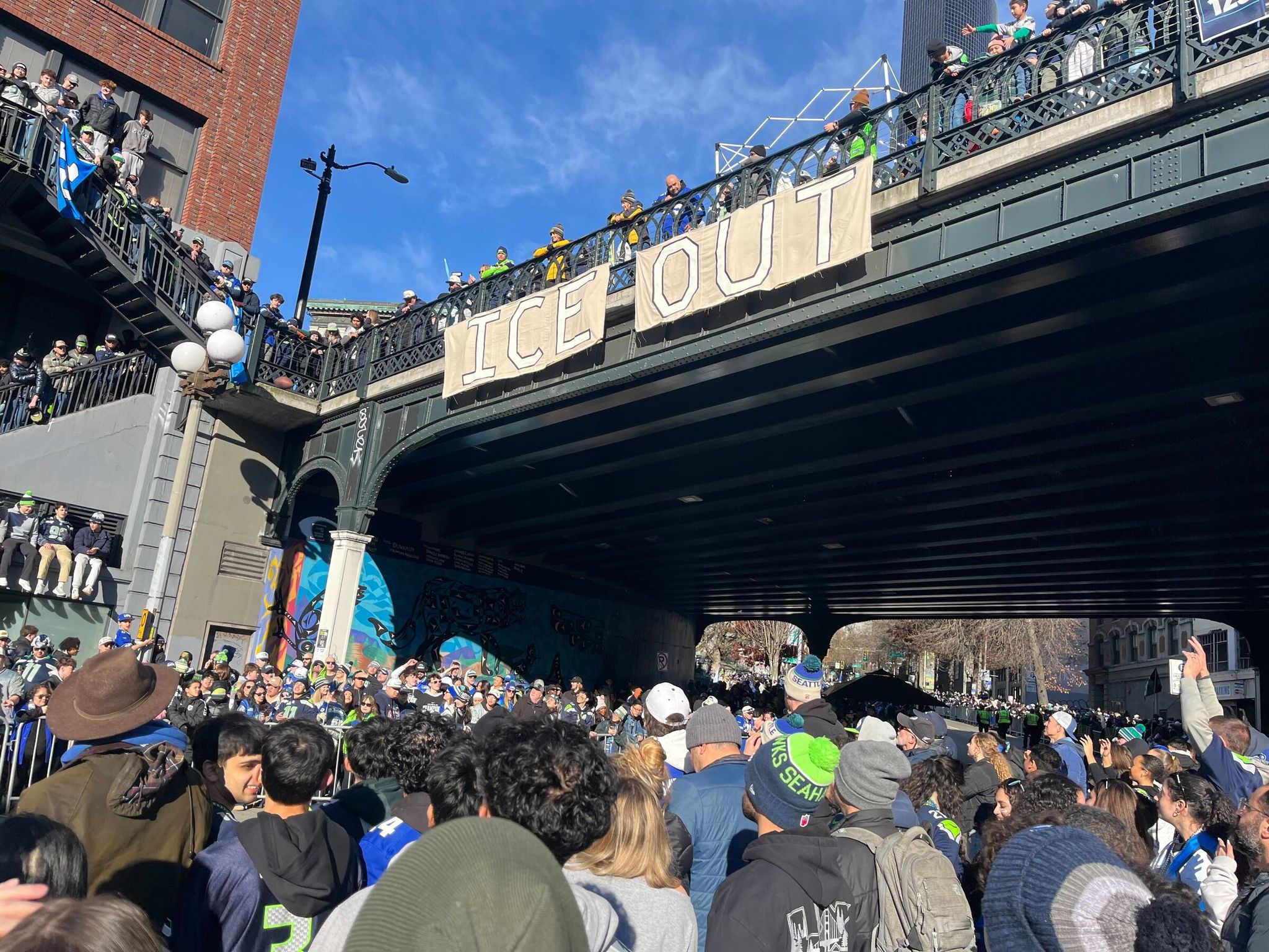 People unfurl a large 'ICE OUT' banner on the Yesler Way overpass above the parade around 10 a.m. on Wednesday. (Kai Uyehara / The Seattle Times)