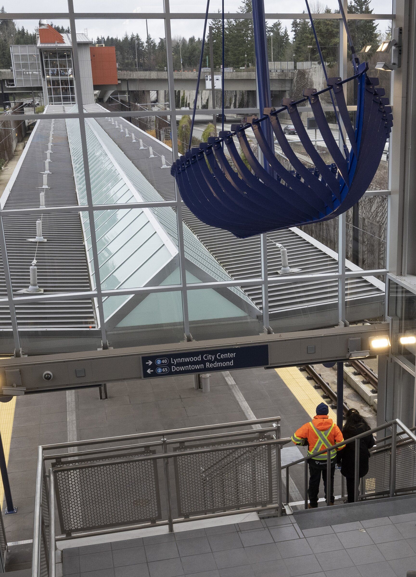 Artwork by Seattle artist Beliz Brother hangs above the Mercer Island station entrance, evoking a boat rocking on the water. Tom Ihlele, Sound Transit facilities manager (left), and Rachel Cunningham, Sound Transit spokesperson, stand below. (Ellen M. Banner / The Seattle Times)