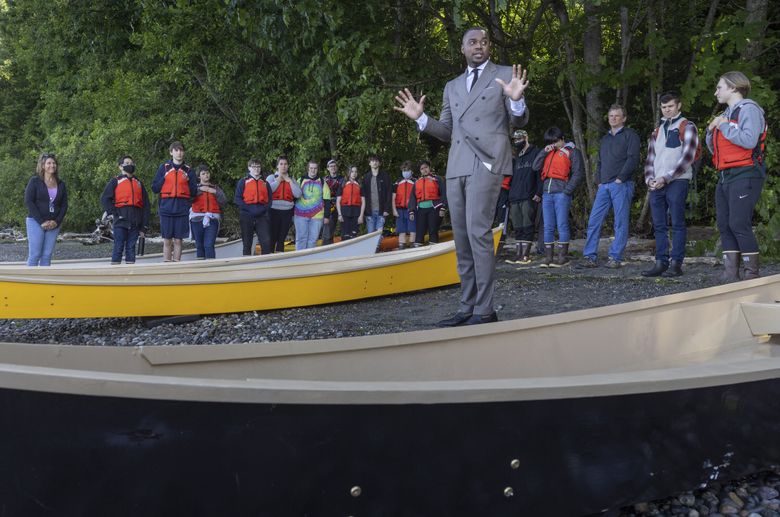 Maritime High School Principal Tremain Holloway speaks to students while standing on the beach at Seahurst Park in Burien next to the four 18-foot ‘Peace Canoes’ the ninth graders built throughout the year as part of their STEM curriculum and maritime training in 2022. (Ellen M. Banner / The Seattle TImes)