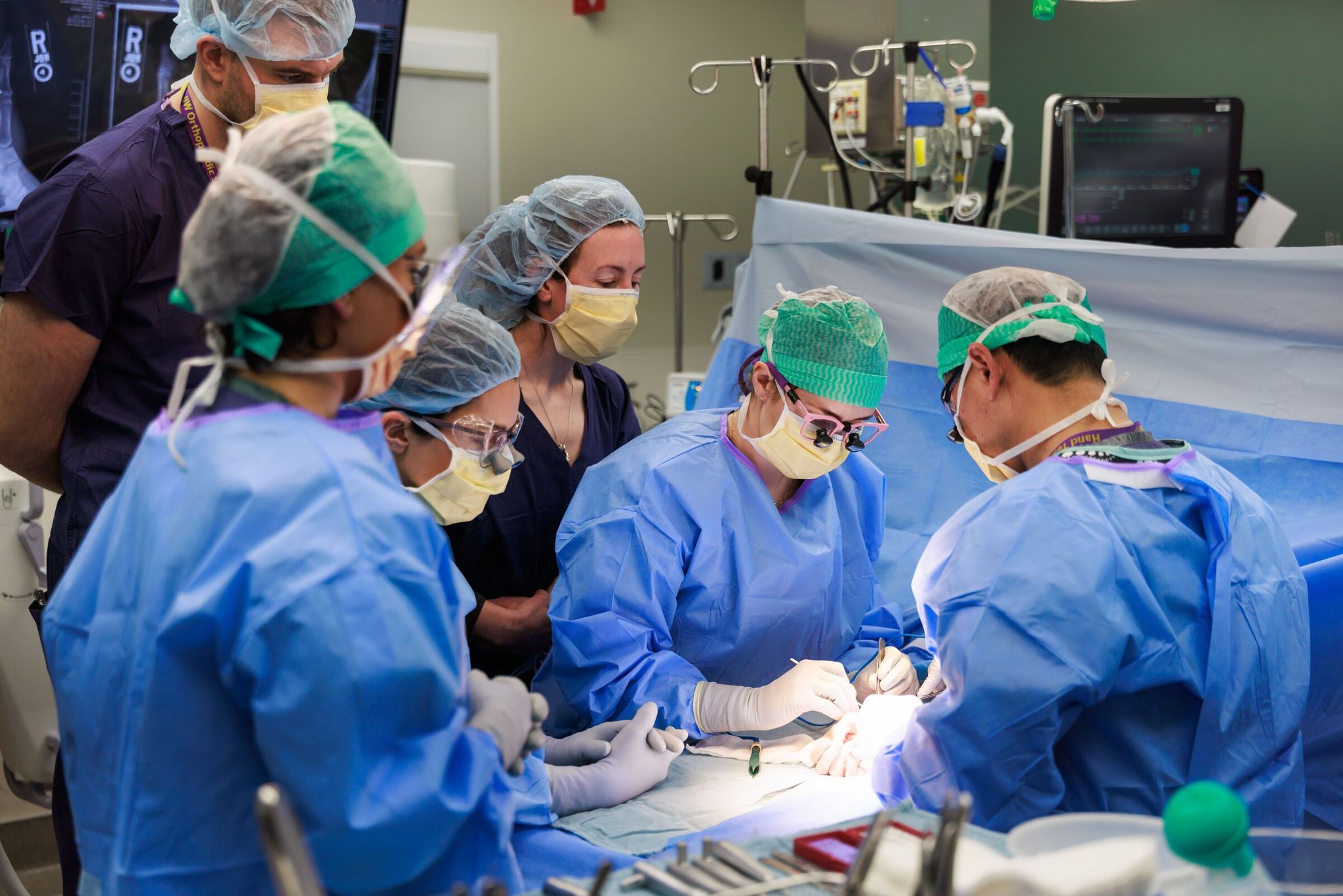 Dr. Brynn Hathaway, in pink glasses, assisted in the thumb joint replacement using a prosthesis last week; next to her is Dr. Emily Hunt, and on the other side of the table is Dr. Jerry Huang, at UW Medical Center – Roosevelt. (Erika Schultz / The Seattle Times)
