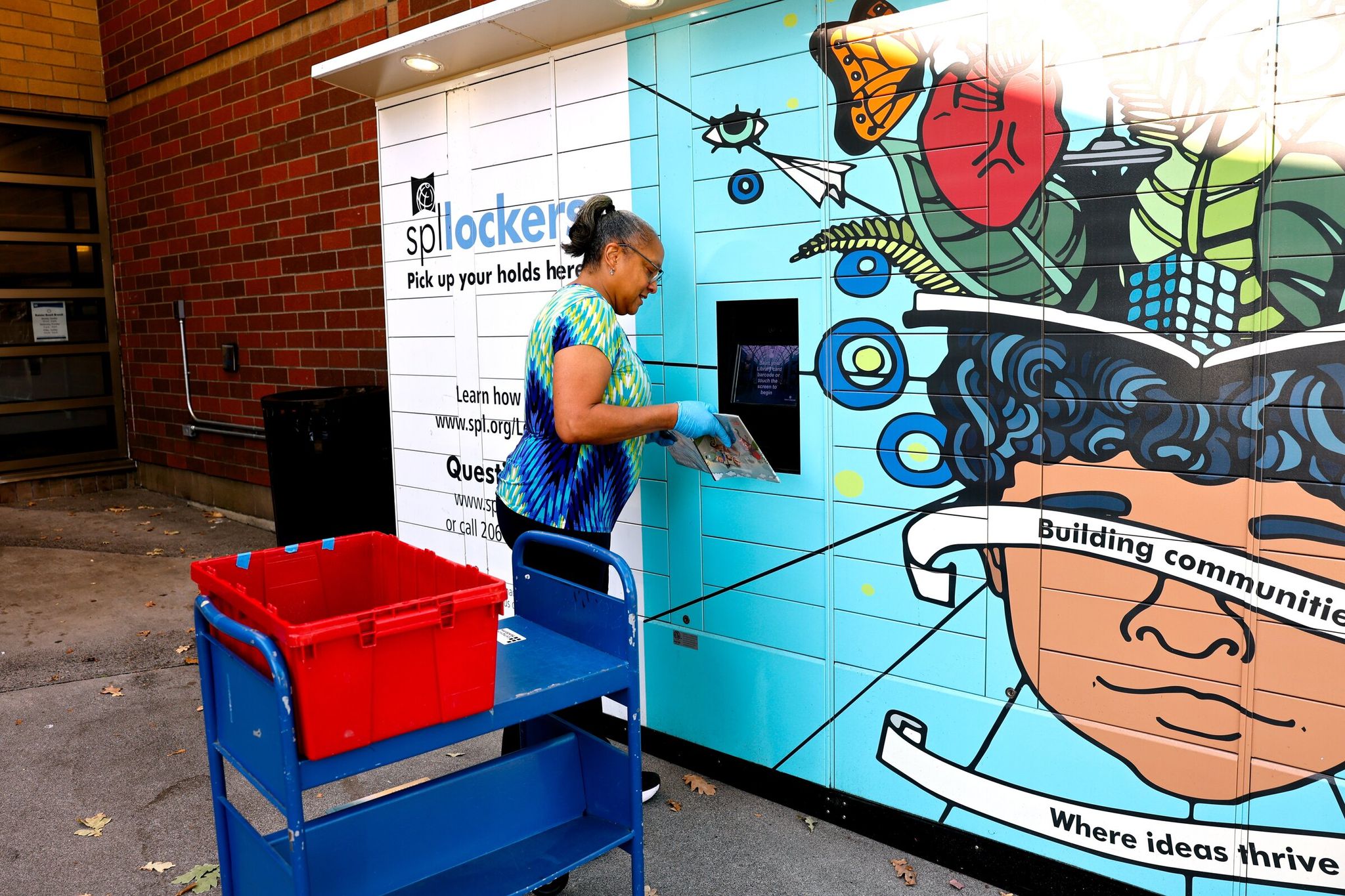 Carlotta Walker, a library staffer, places books in lockers at the Seattle Public Library’s Rainier Beach branch. The Seattle City Council committee increased the size of the summer library ballot measure by nearly $70 million to cover additional maintenance, hours, staffing and collections. (Karen Ducey / The Seattle Times)