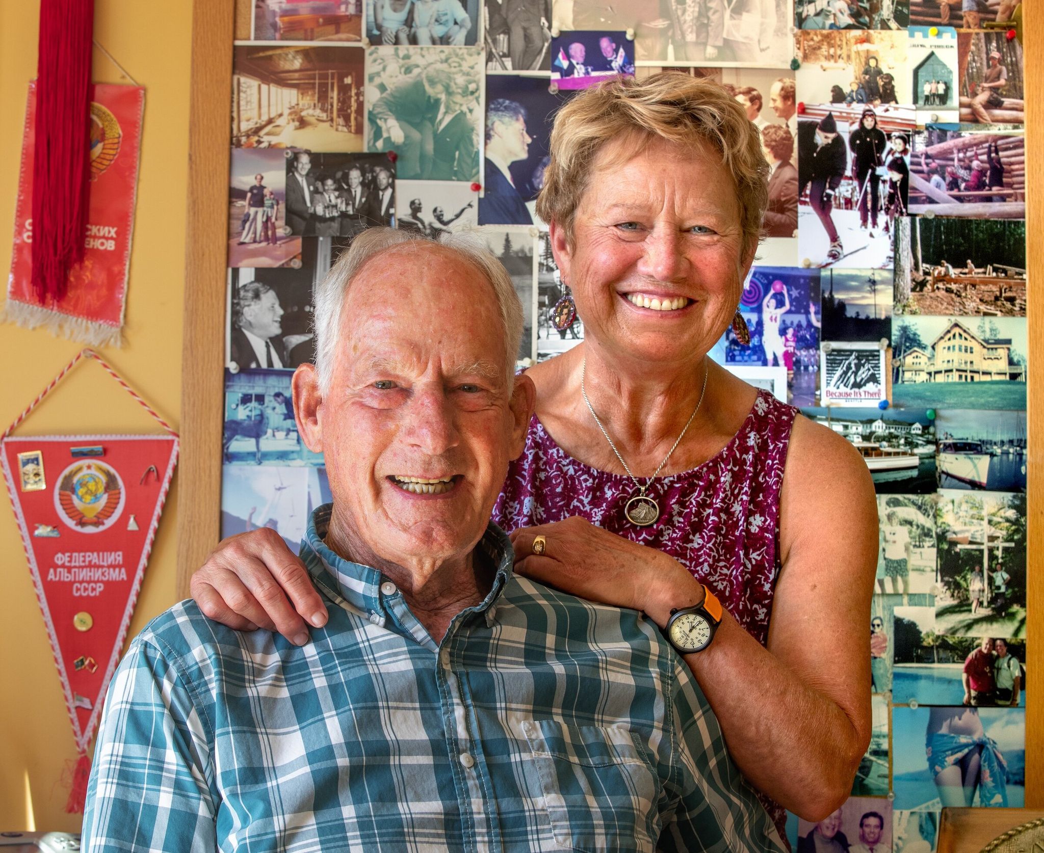 Jim Whittaker, American climber and mountain guide, and his wife Dianne Roberts, in Port Townsend in 2019. The couple are photographed in front of a gallery of photos showing Whittaker with members of the Kennedy family, including an image of Whittaker teaching Jacqueline Kennedy and John F. Kennedy Jr. how to ski (top right). (Mike Siegel / The Seattle Times, 2019)