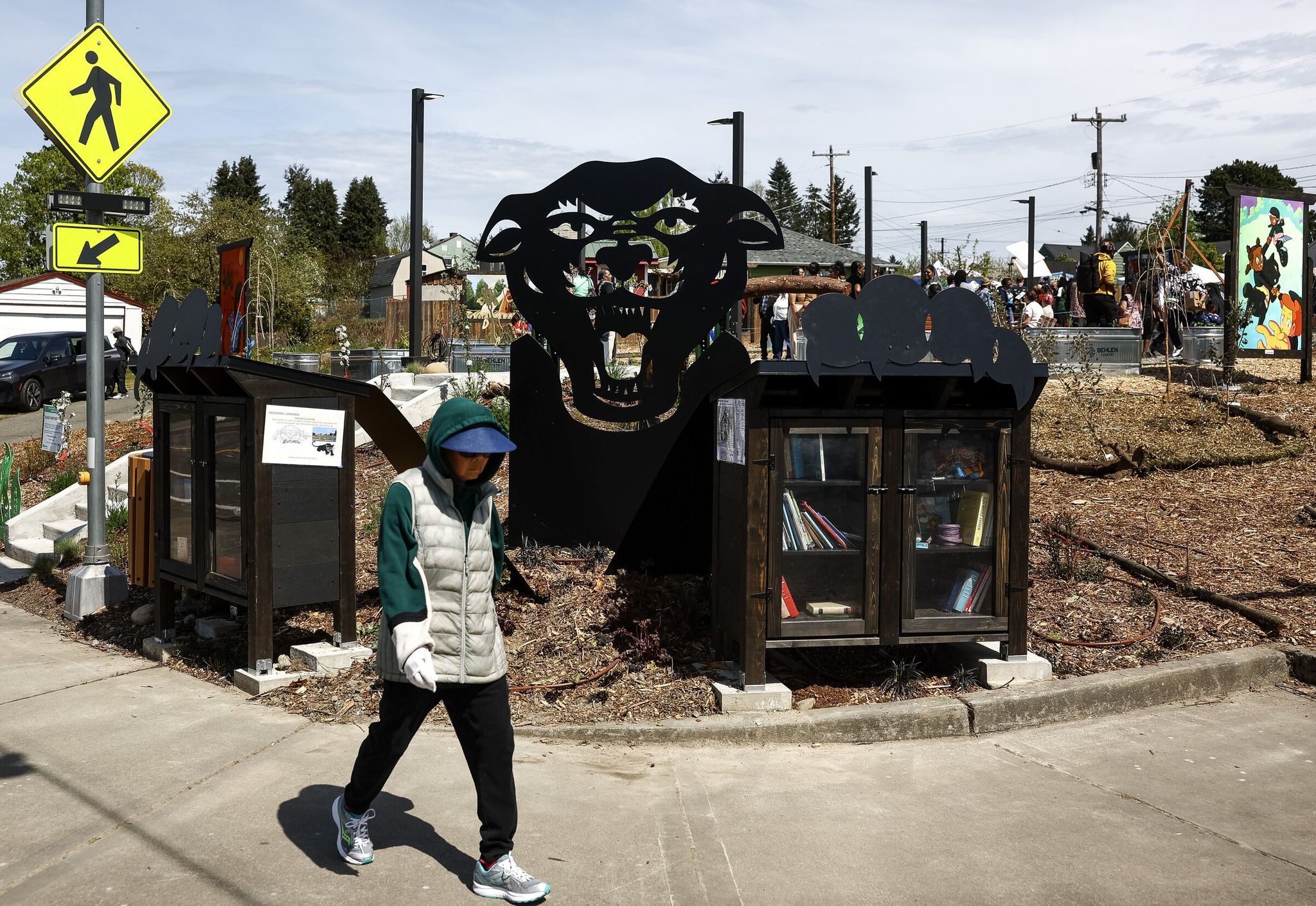 A pedestrian walks past a metal art piece framing a small free library and food pantry during the Black Panther Park opening ceremony on Sunday. (Nick Wagner / The Seattle Times)