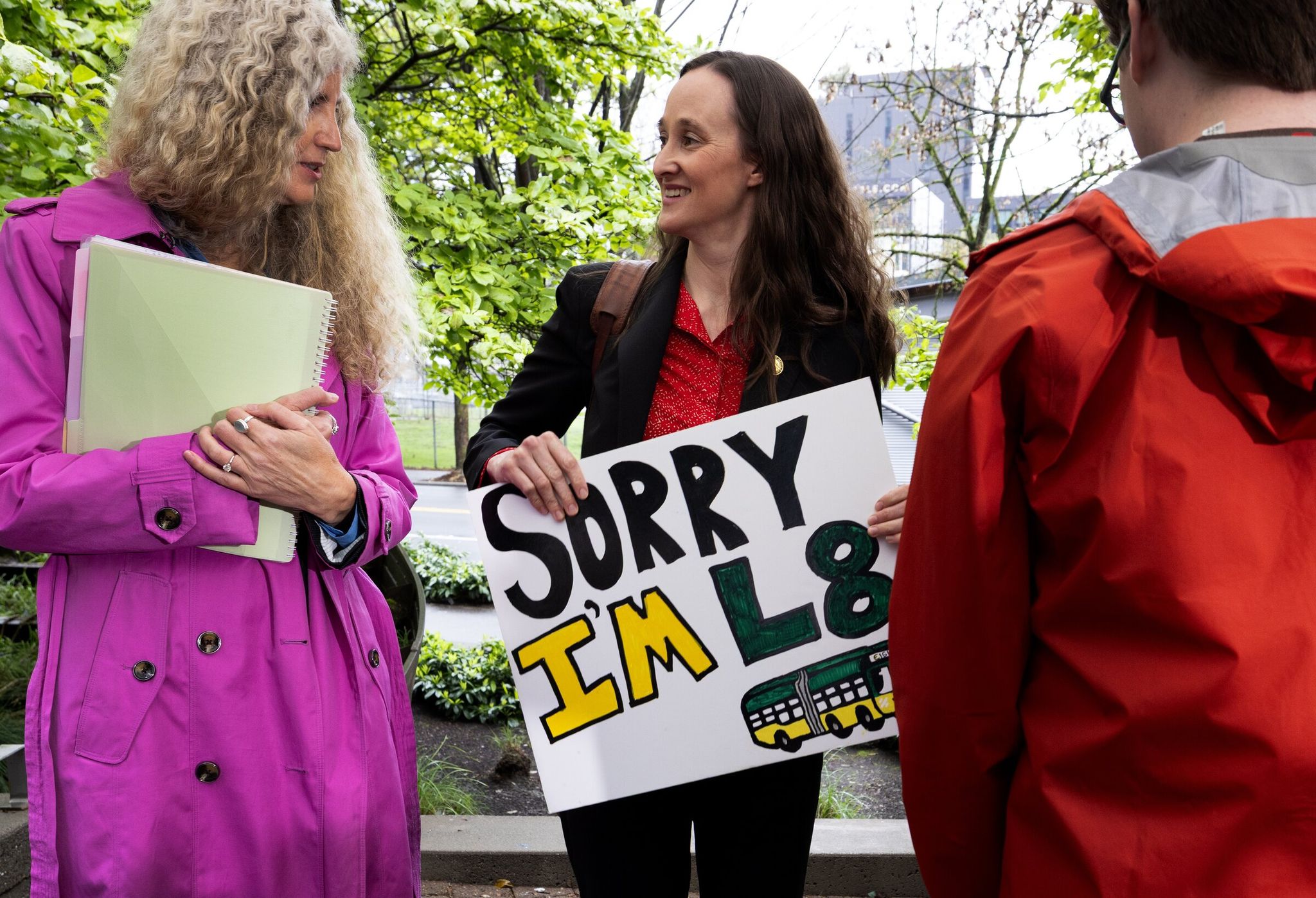 Mayor Katie Wilson, center, who brought her own sign, chats with Angela Brady, interim director of the Seattle Department of Transportation, at a press event, Wednesday, April 22, 2026, in Seattle’s Denny Triangle. Wilson went on to announce her plan to re-order Denny Way to help move the Route 8 bus, also known as “Late 8.” (Ken Lambert / The Seattle Times)