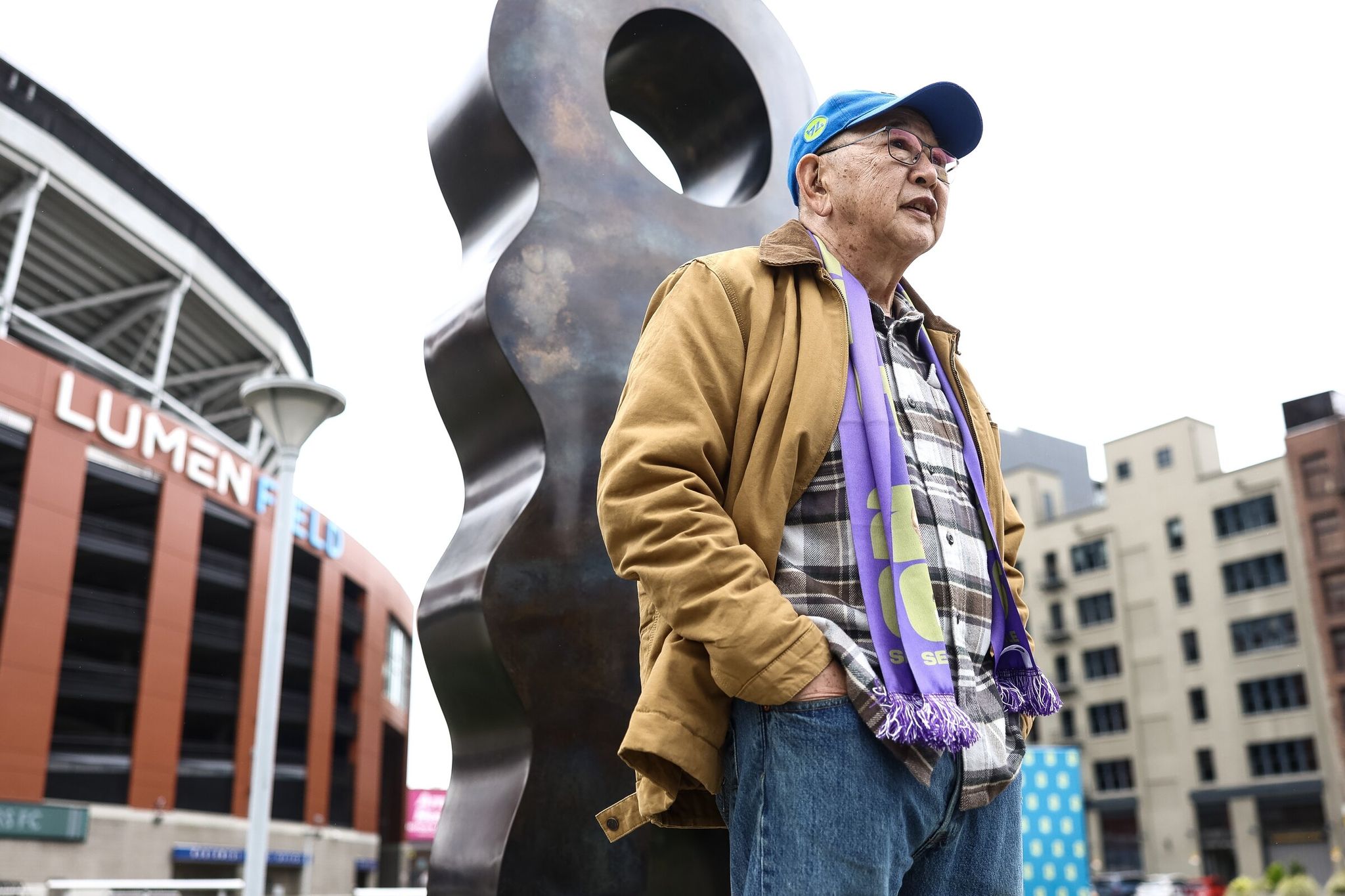 Local artist Gerard Tsutakawa stands next to his 'Vital Spirit' sculpture after its unveiling in front of Lumen Field on Monday. (Nick Wagner / The Seattle Times)