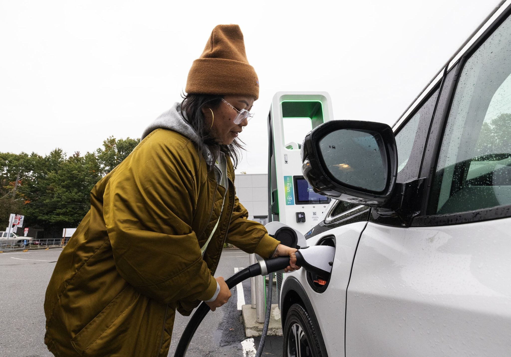 Meesa Pedrozo at a Lower Queen Anne charging station plugs into her EV, Monday, Oct. 9, 2023 in Seattle. (Ken Lambert / The Seattle Times)