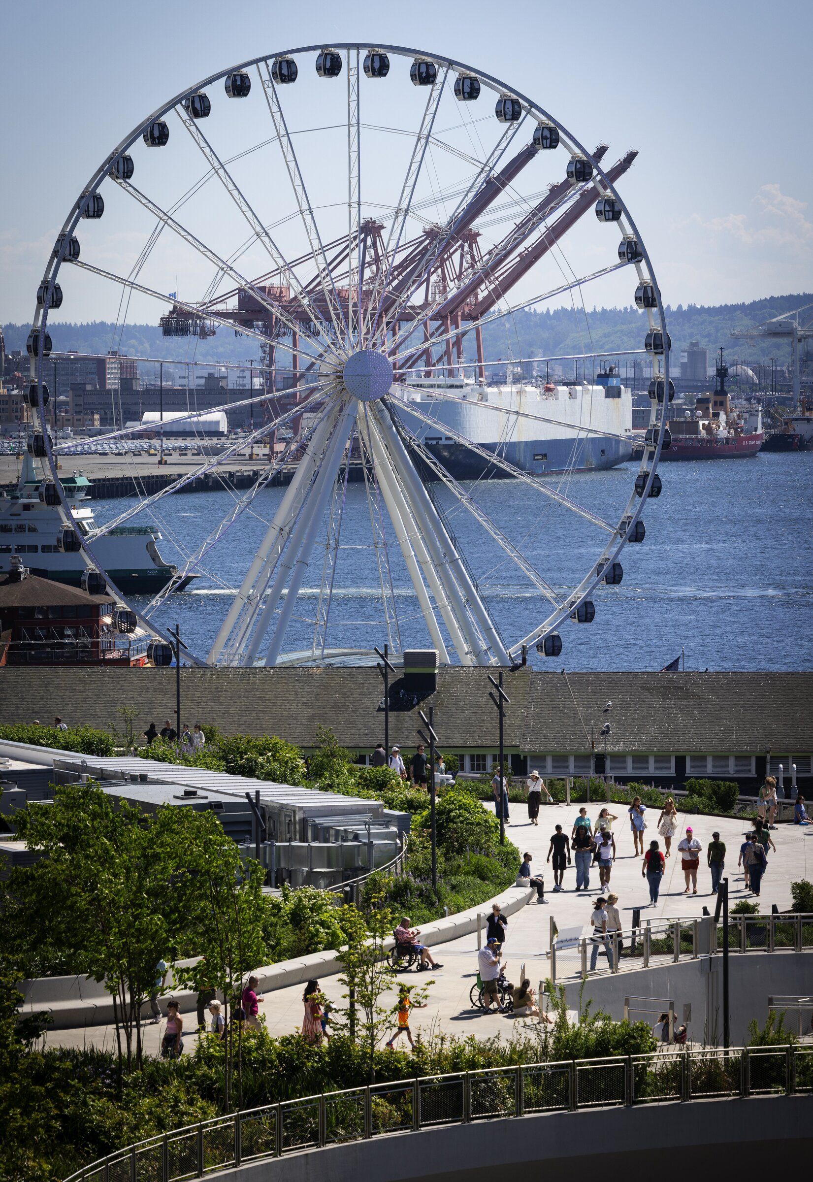 The Seattle Great Wheel provides a backdrop as people cross the Overlook Walk on the waterfront on Sunday afternoon as summerlike temperatures climbed into the upper 70s. (Ken Lambert / The Seattle Times)