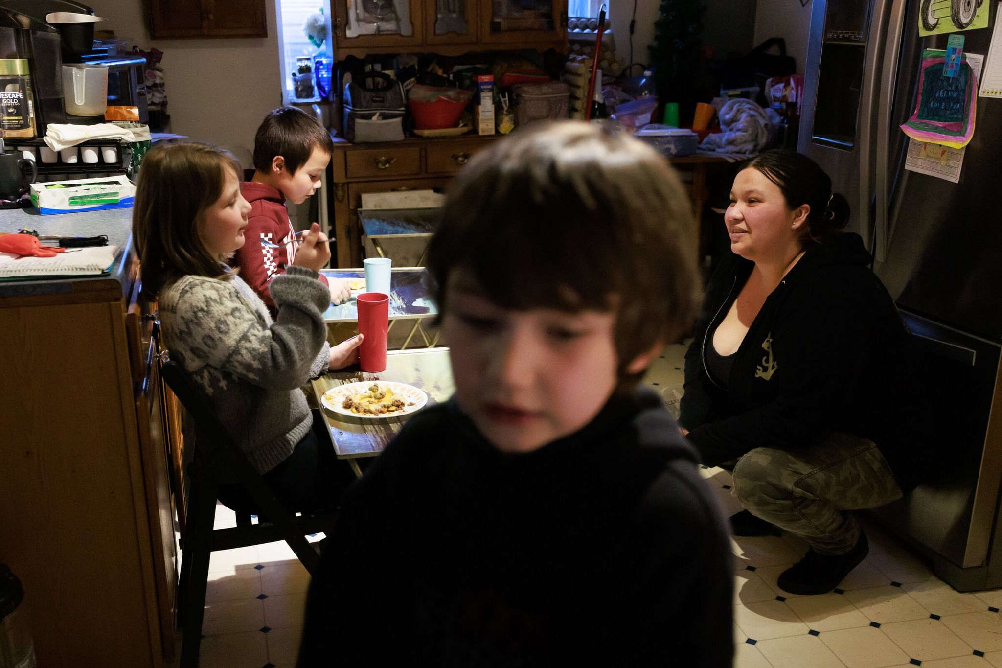 On the right — Michelle Lane talks with her children — Oliver, 6; Amelia, 9; and Thomas, 7 — during dinner at her parents’ home in Auburn, where they have shared a room since leaving their apartment. As of May, Lane said her family had not received a penny in government aid. They hope to move into a new apartment soon. (Erika Schultz / The Seattle Times)