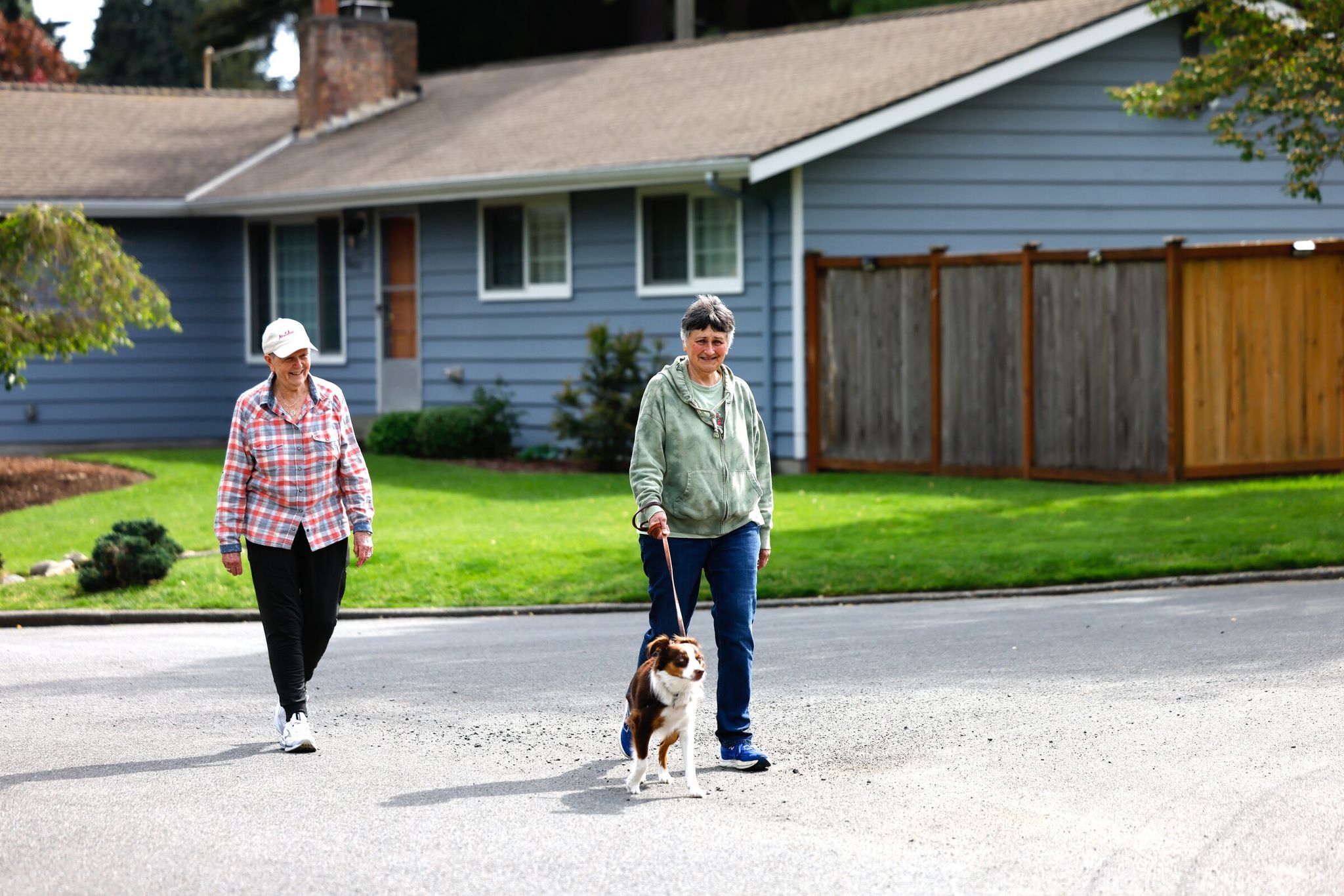 Pam Jensen (left) and Mary Jack walk their 9-month-old puppy Cora Blue down a street in Shoreline’s Meridian Park neighborhood in May. (Karen Ducey / The Seattle Times)