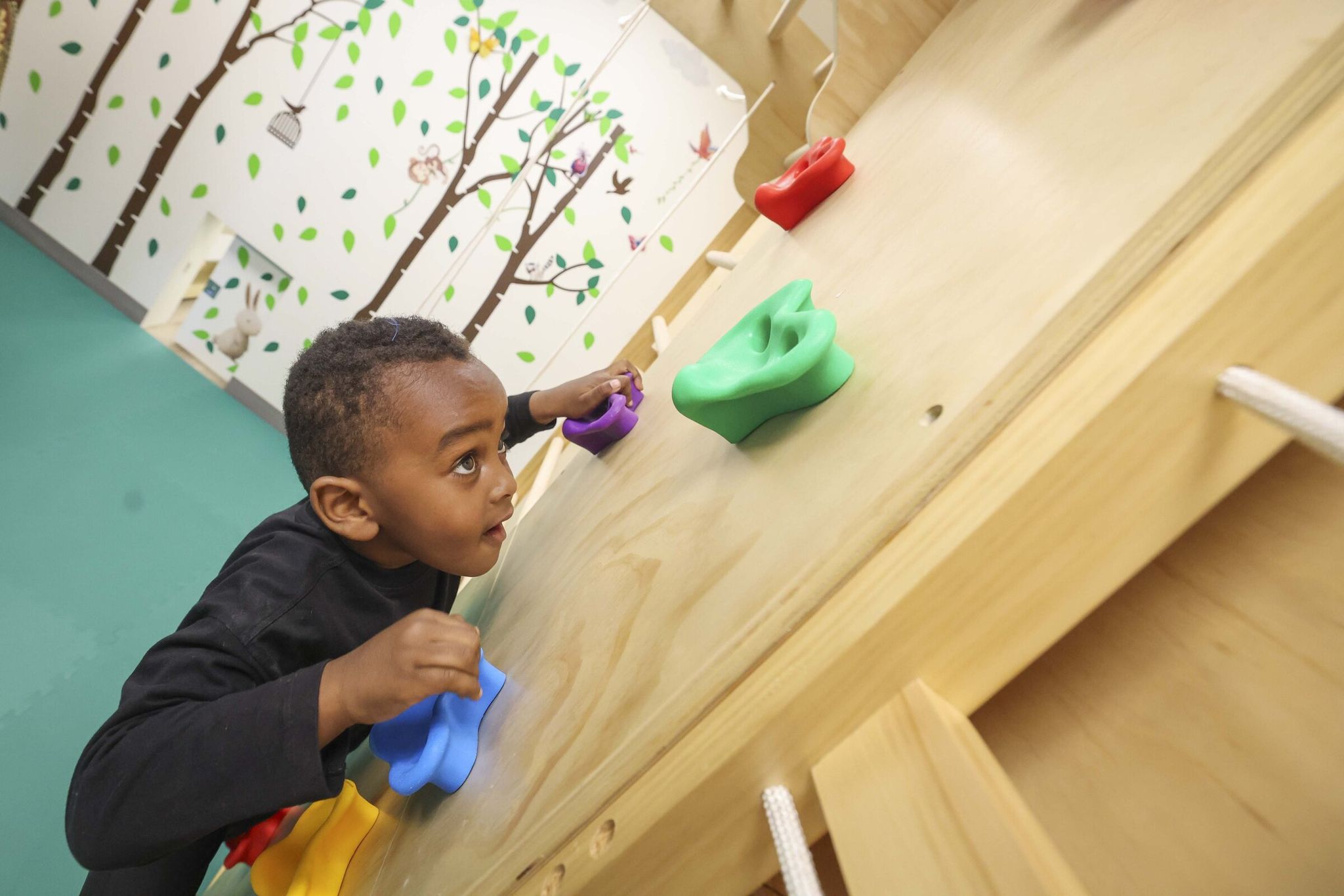 Kuhafi “Sufi” Sharif, 4, climbs a wall inside the active sensory playroom during the center’s grand opening. (Ivy Ceballo / The Seattle Times)