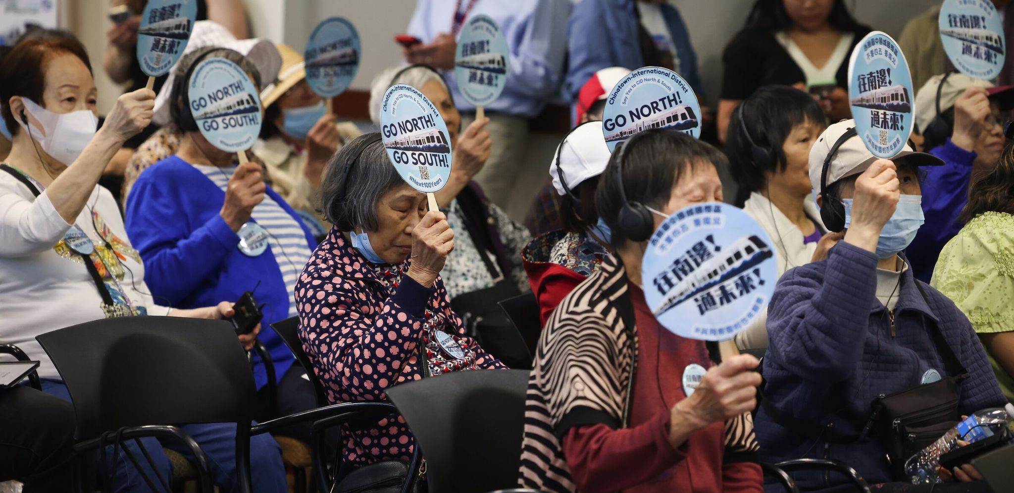 Residents of the Chinatown-International District hold signs urging Sound Transit to build the future station several blocks south rather than next to the historic Chinatown gates. Many also advocated restoring the Graham Street station. (Ken Lambert / The Seattle Times)