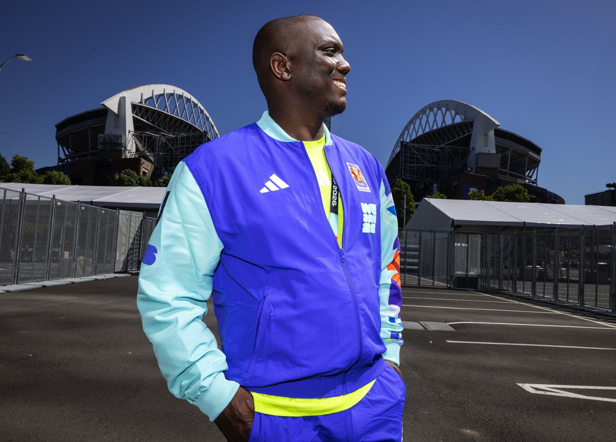 Oscar Singini, of Everett, models his FIFA World Cup volunteer uniform after picking it up on May 27. He stands outside Lumen Field, which will be rebranded to Seattle Stadium for the duration of the World Cup. A Malawian, Singini said he’s cheering on African teams, including Egypt, and has tickets for that country’s match with Belgium on June 15. (Ken Lambert / The Seattle Times)