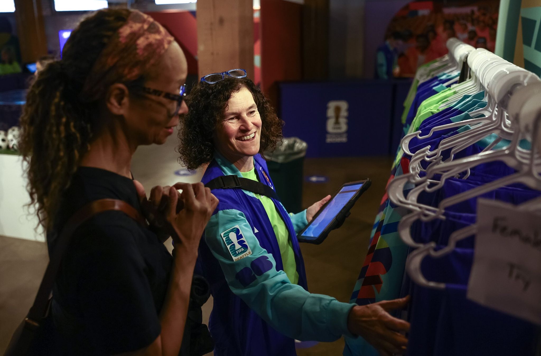 Jennifer Hayes, right, helps fellow FIFA World Cup volunteer Suzzanne Lacey find the right size for a volunteer uniform on May 20 in Seattle. (Nick Wagner / The Seattle Times)