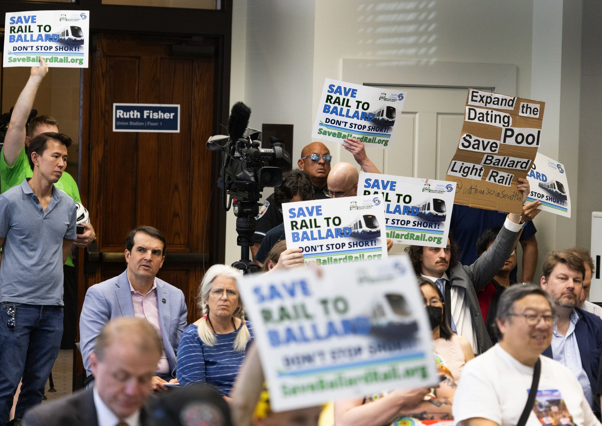 People hold signs during public remarks before the Sound Transit Board voted on alignment related to future stations on Thursday, May 28, 2026, in Seattle. (Ken Lambert / The Seattle Times)