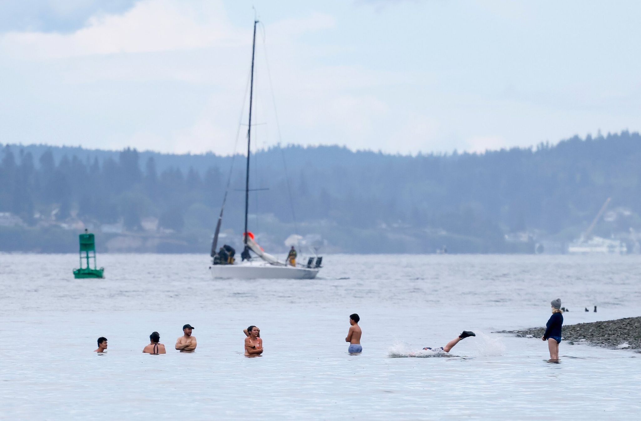 Hardy souls brave the cold temperatures of the waters just off Golden Gardens as a sailboat makes it way around the point Saturday in Seattle. (Jennifer Buchanan / The Seattle Times)