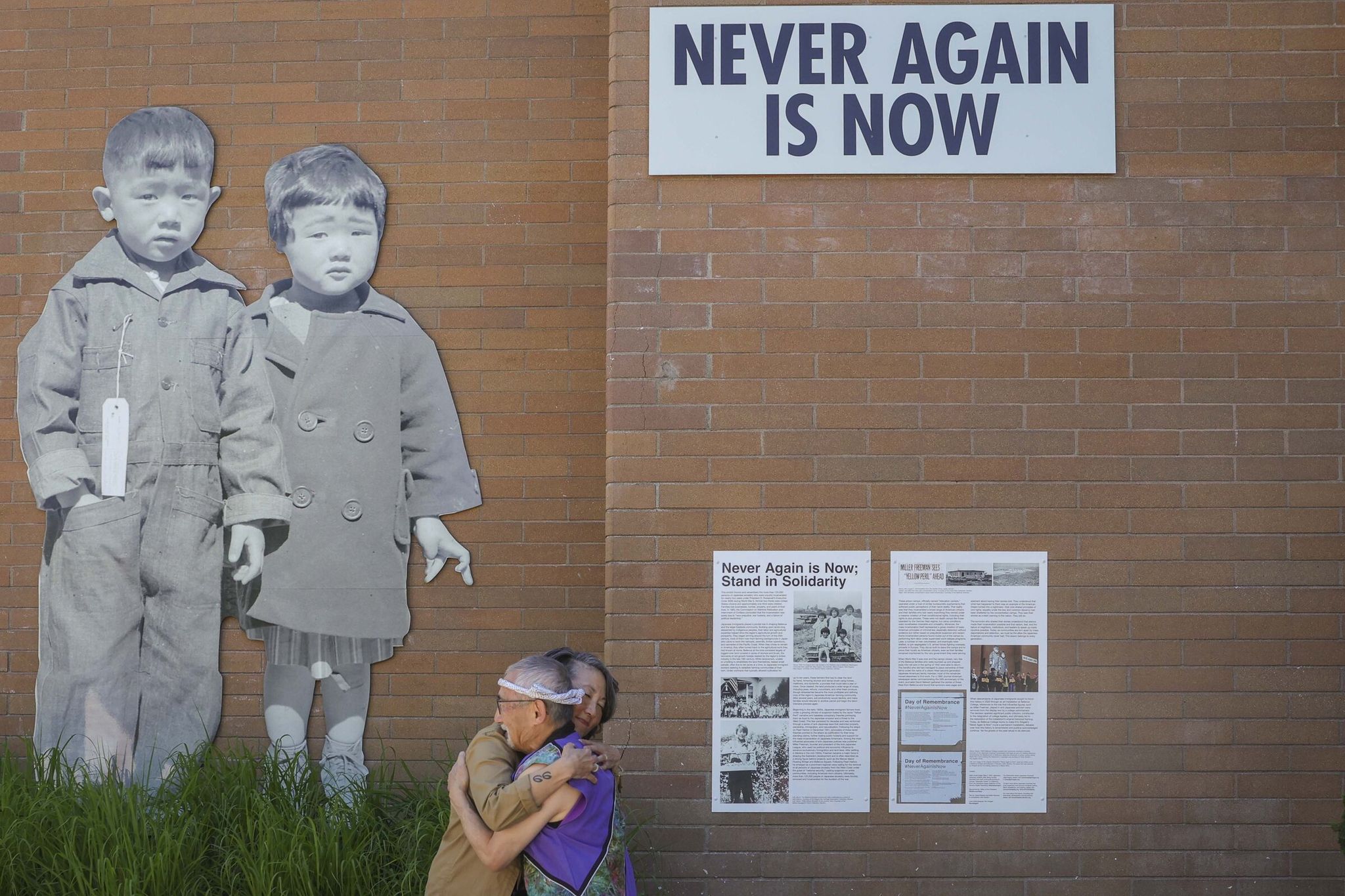 Artist and activist Erin Shigaki, left, and Stan Shikuma, with Japanese American Citizens League and Tsuru for Solidarity, share a moment following the unveiling of permanent installation “Never Again is Now” by Shigaki at Bellevue College in Bellevue on Thursday. (Ivy Ceballo / The Seattle Times)