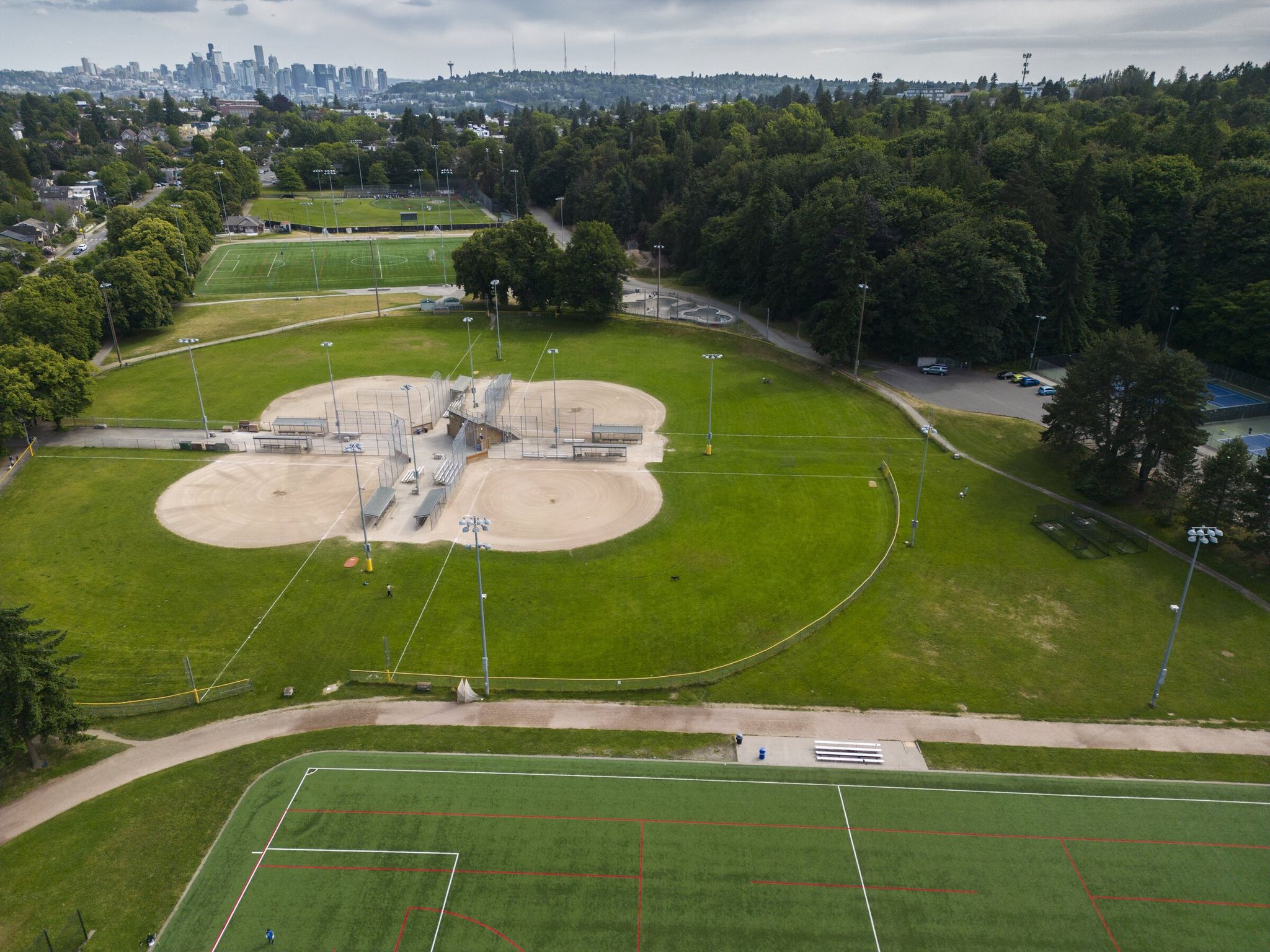 Lower Woodland Park playfields can be seen looking south toward the Seattle skyline in June 2025. Tennis courts are at center right. The wooded area of the park at top right has trails, an off-leash dog park, picnic areas, lawn bowling, horseshoe pits and many other outdoor activities available to the public. (Ellen M. Banner / The Seattle Times)