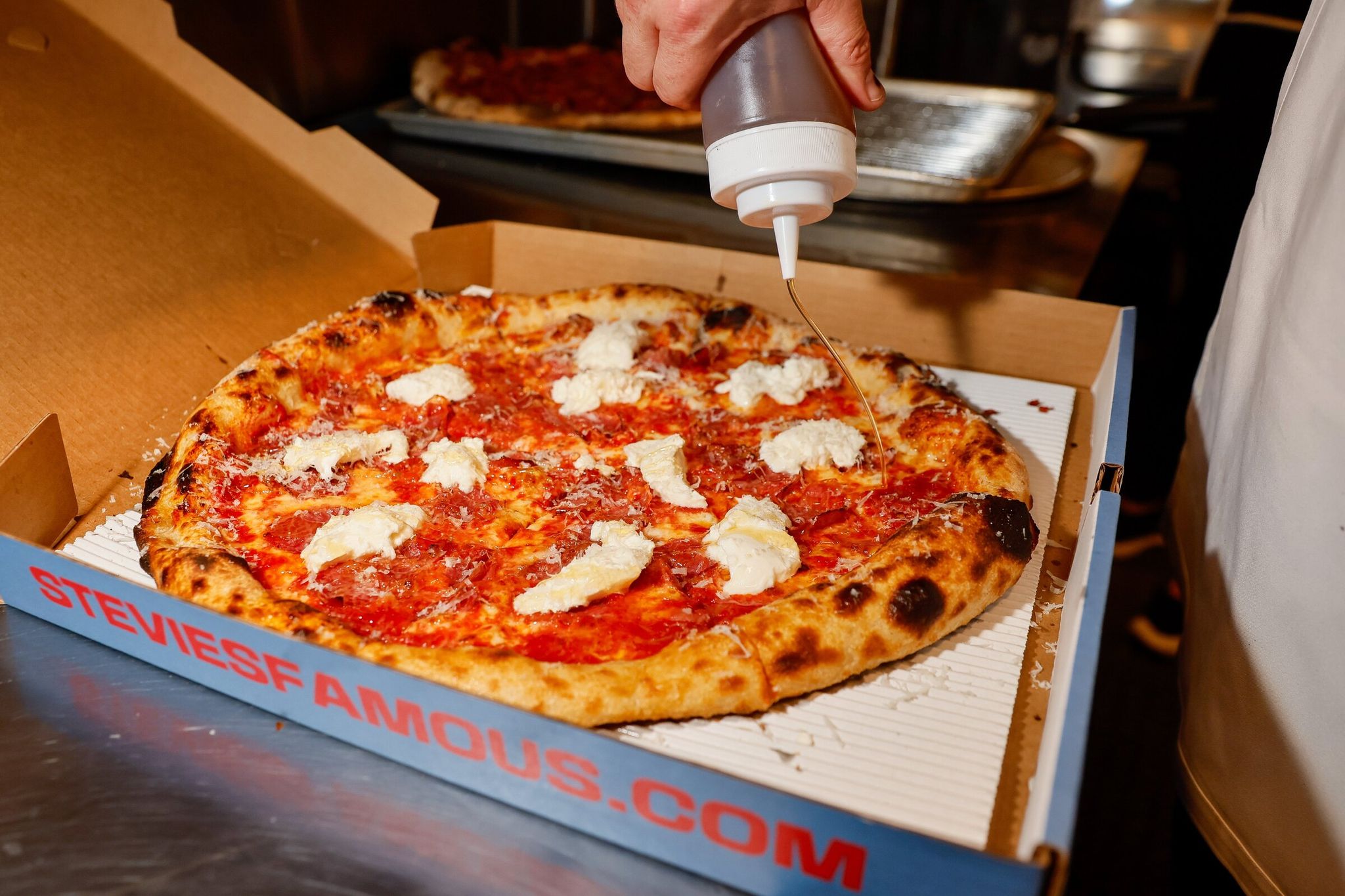 Stevie’s Famous co-owner Shane Abbott drizzles hot honey on an OG Normie pizza at the original Burien pizzeria in this 2023 photo. (Jennifer Buchanan / The Seattle Times)