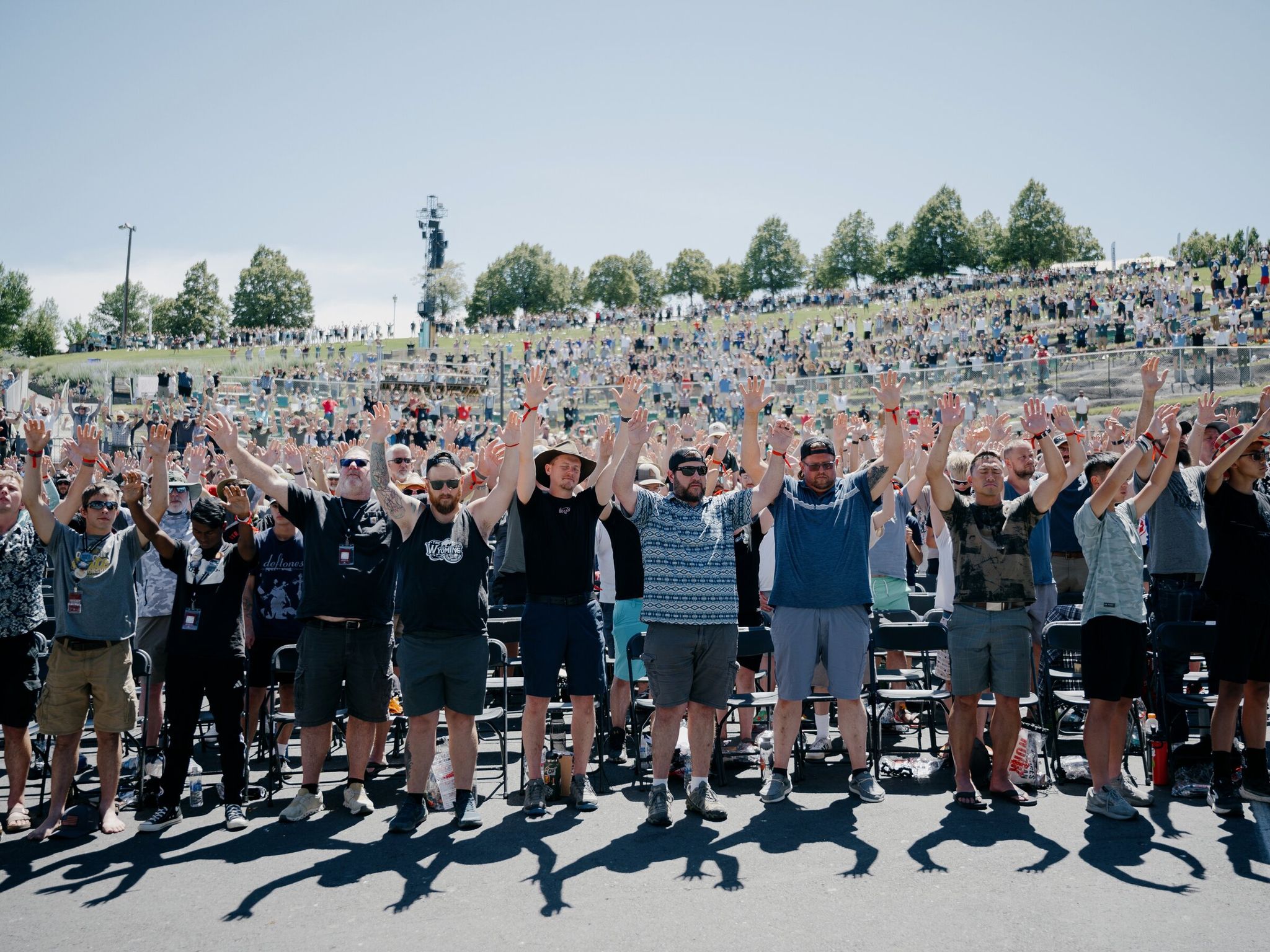 Men respond with raised arms during a morning sermon at Freedom Con, held over Father’s Day weekend, at the Gorge Amphitheatre outside George, Wash., June 20. More than 4,500 men gathered in central Washington for a celebration of Christianity and patriotism that included an obstacle course, tire changing lessons and exhortations from speakers to run for office, to have more babies and to reject “woke secular gay paganism.” (Grant Hindsley / The New York Times)