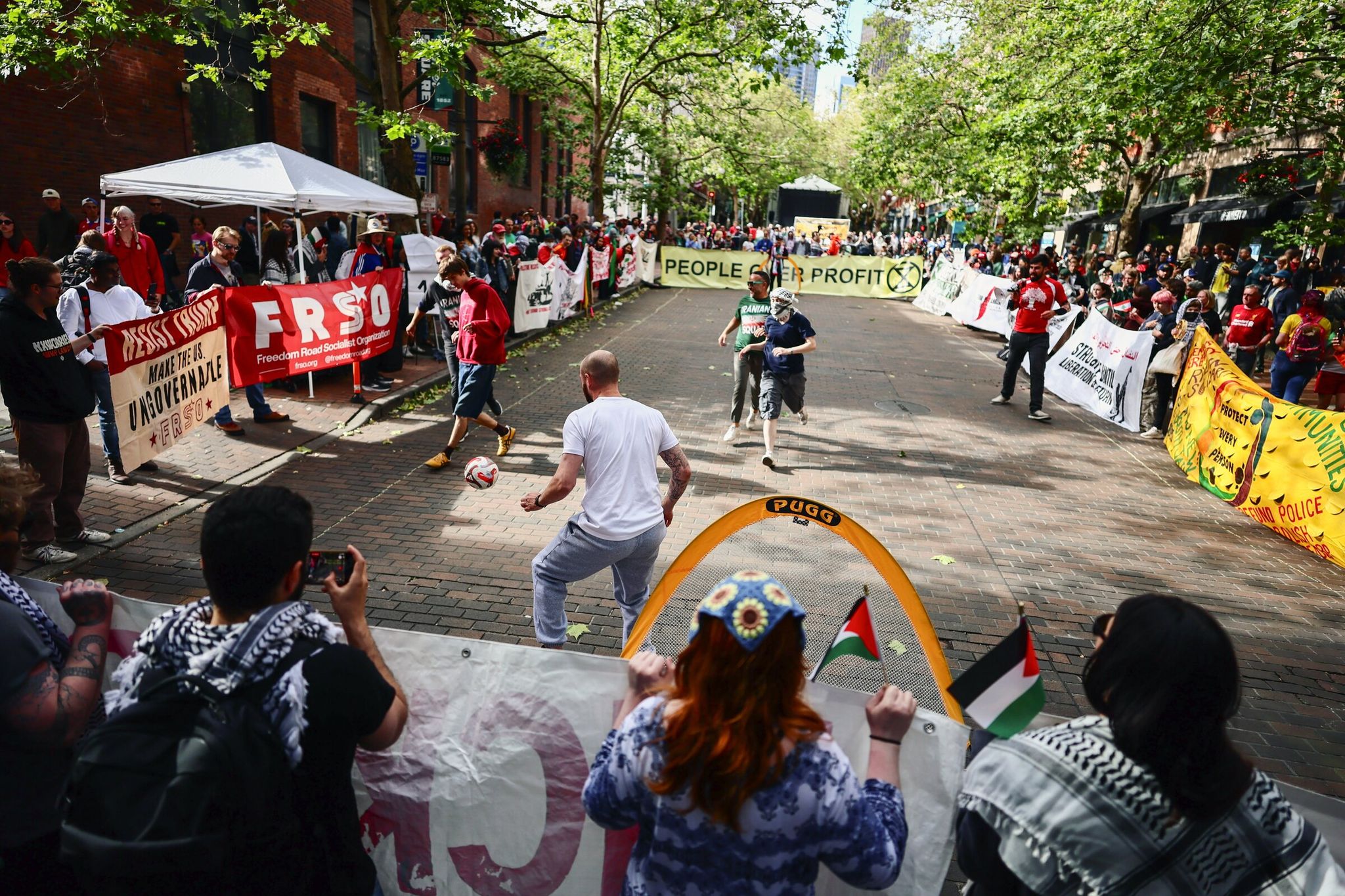 Protesters play 3-on-3 football to demonstrate “People matter more than profit” on Occidental Avenue South in Pioneer Square on Friday, June 26, 2026, ahead of the FIFA World Cup group stage match between Iran and Egypt. (Kevin Clark / The Seattle Times)