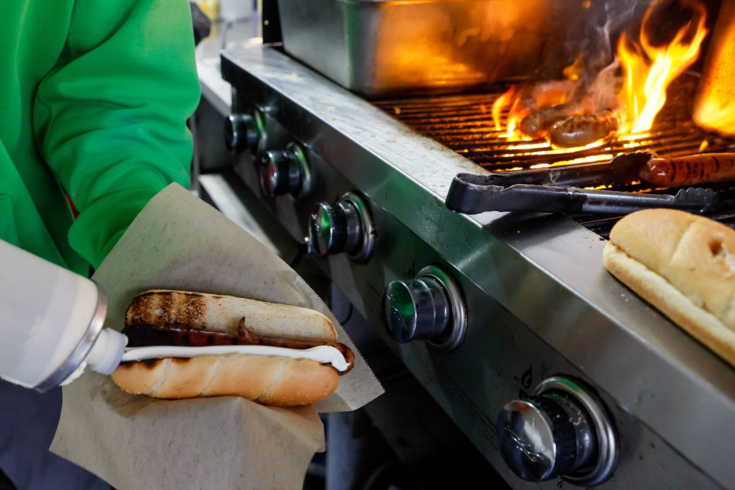A line of cream cheese drips along the hot dog as Payden Varamini prepares a Seattle-style hot dog for a customer before the start of a playoff match between the Sounders and Houston in 2024 outside Lumen Field. (Jennifer Buchanan / The Seattle Times)