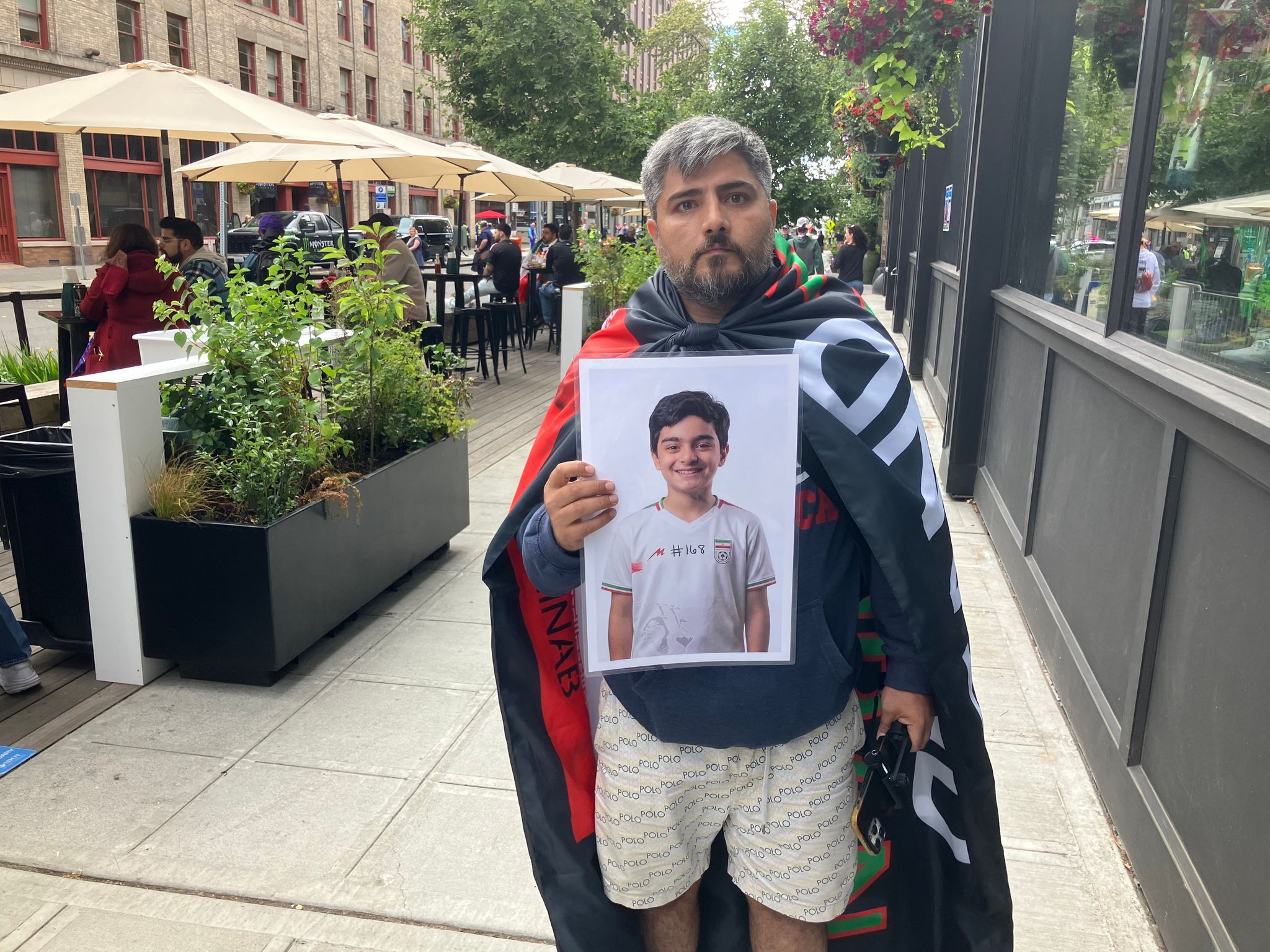 Beza, who as a youth played for Iran’s youth national teams, carries an Iran flag and a photo of a boy killed during the war with the United States outside “Seattle” Stadium before the World Cup match on Friday. (Daniel Bikman / The Seattle Times)
