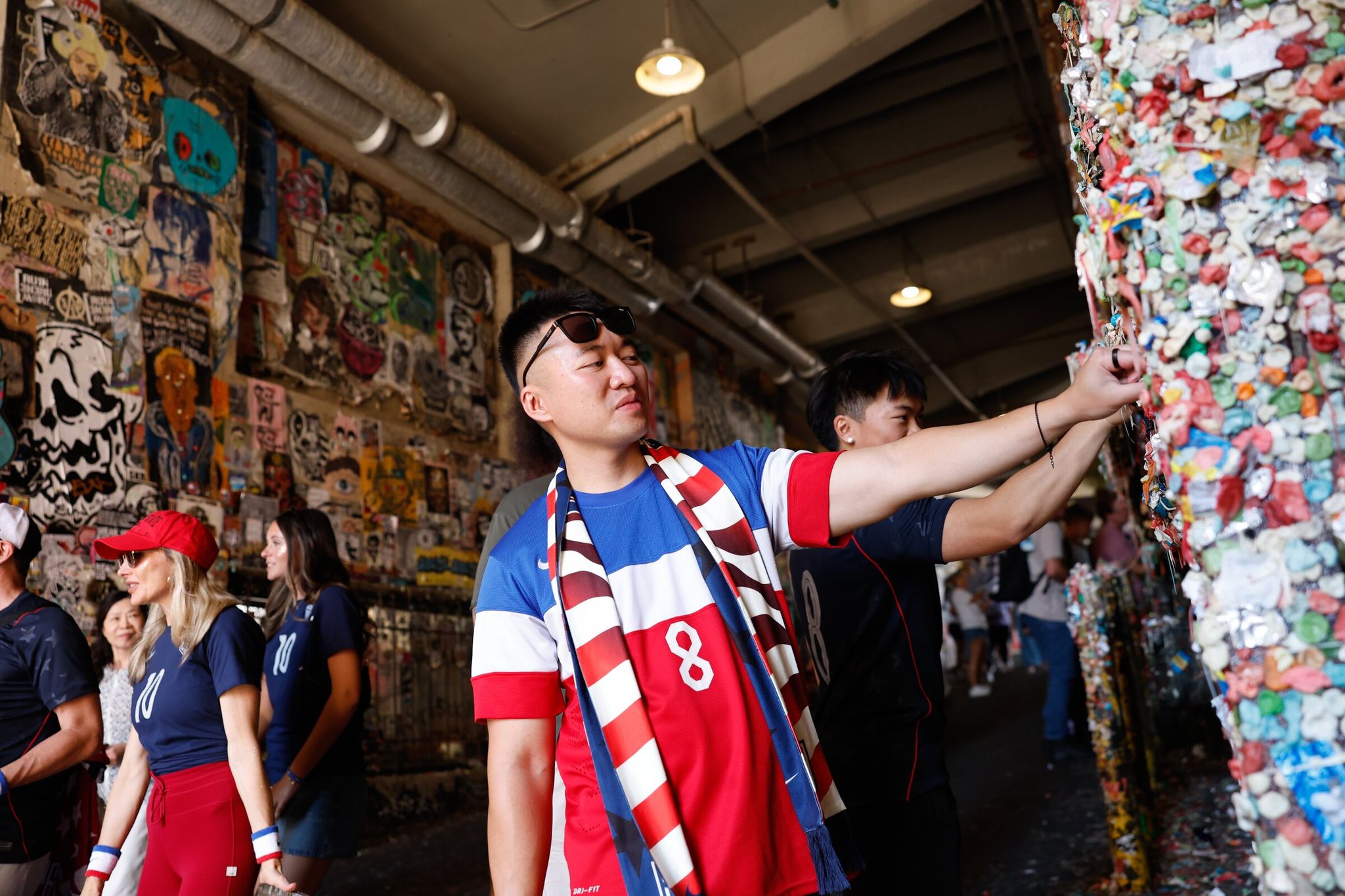 Vi Khong from Denver puts chewing gum on the “gum wall” at Pike Place Market before the round of 16 match between the USA and Belgium in Seattle on Monday. (Karen Ducey / The Seattle Times)