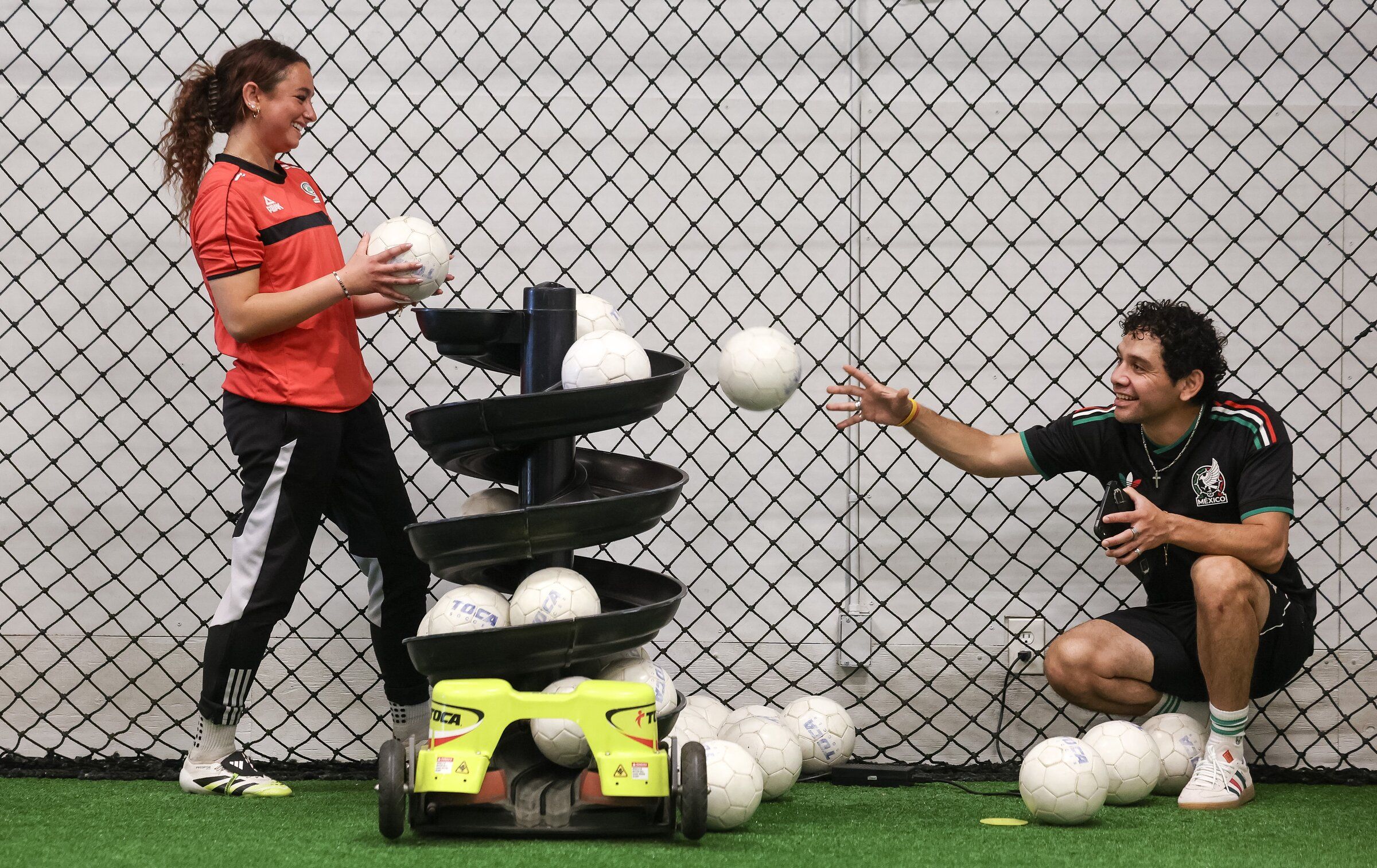 Zjada Baydass and Jose Gomez, the head coach at TOCA Soccer Center in Redmond, reload a ball machine last month. (Nick Wagner / The Seattle Times)