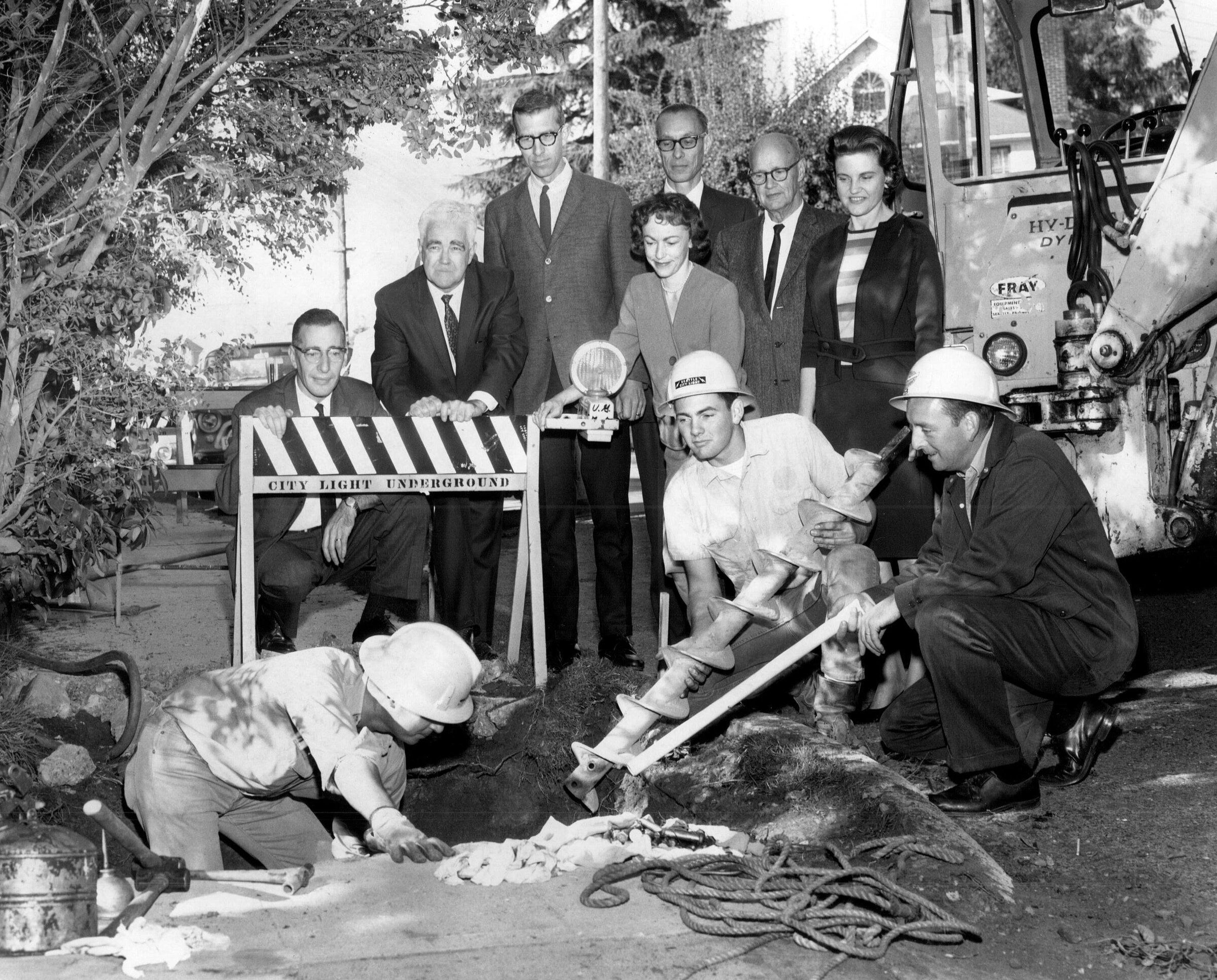 In October 1966, City Light workers Ken Peterson (left) and George Chamberlain, along with foreman Gene Whalen (right), install a drilling machine as Laurelhurst neighbors gather for the occasion. (Vic Condiotty / The Seattle Times)