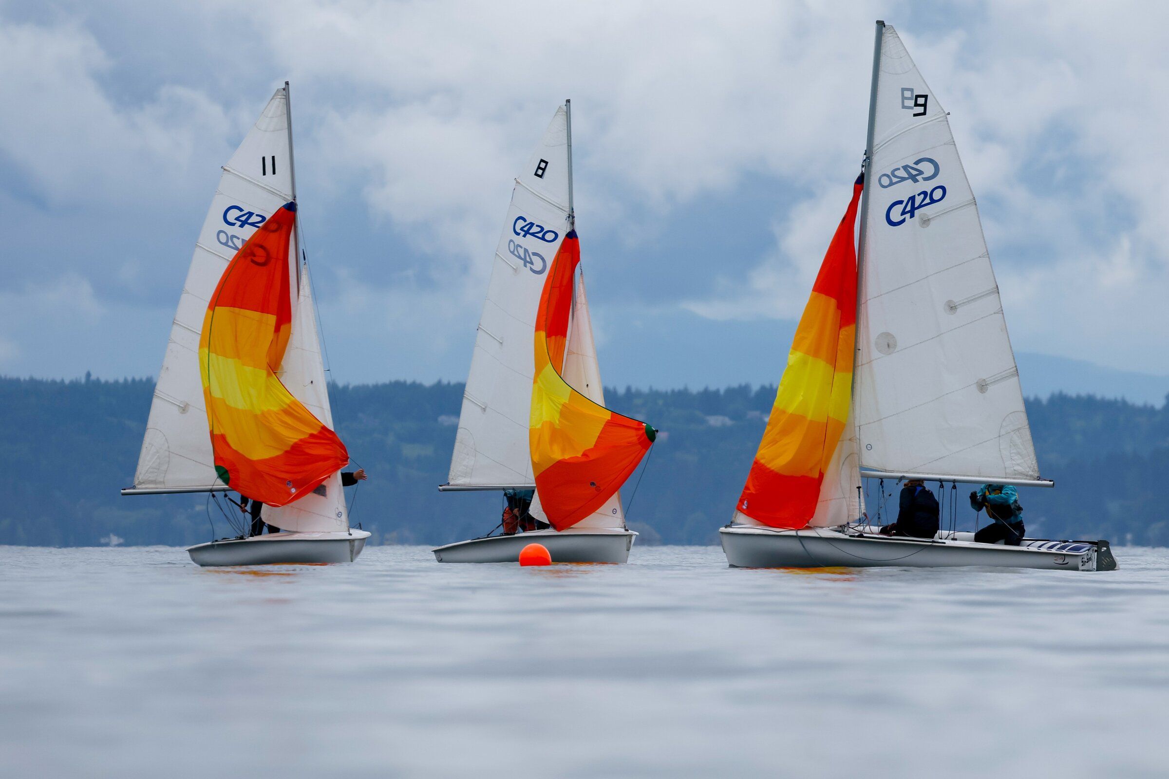 Dramatic storm clouds obscure the Olympic Mountains as small sailboats unfurl colorful spinnakers during practice maneuvers near Shilshole on June 6, 2026, in Seattle.  (Jennifer Buchanan / The Seattle Times)