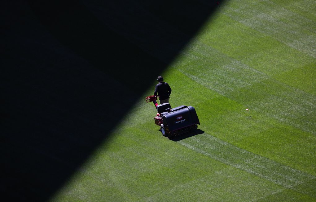 A groundskeeper steers an aerator toward the giant shadow cast by T-Mobile Park’s retractable roof. The roof covers nearly 9 acres when closed. (Ken Lambert / The Seattle Times)