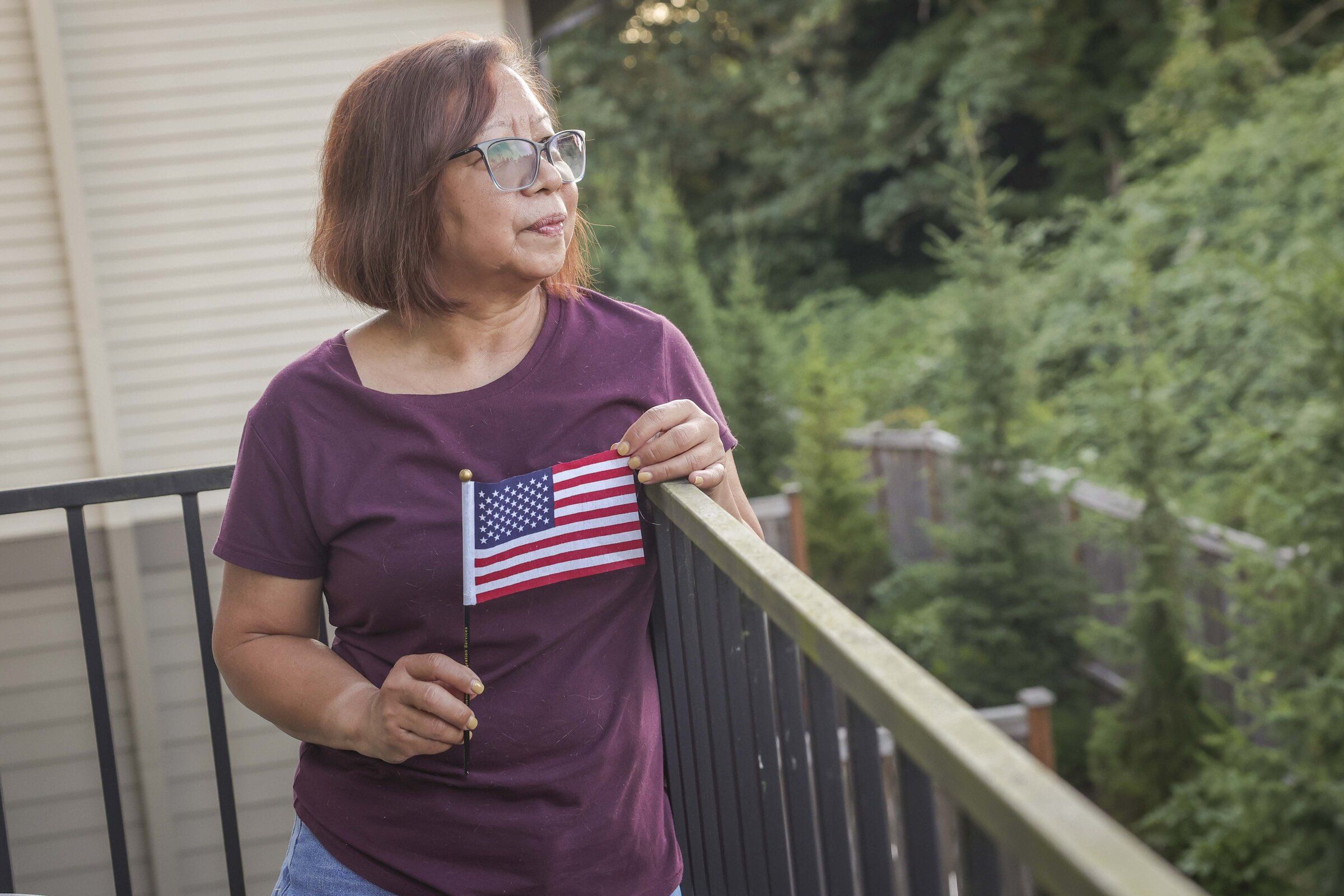 Lewelyn Dixon looks out over her balcony as she holds an American flag she received during her United States citizenship ceremony. A little over a year after she was released from the Northwest ICE Processing Center in Tacoma, Dixon became a naturalized citizen. (Ivy Ceballo / The Seattle Times)