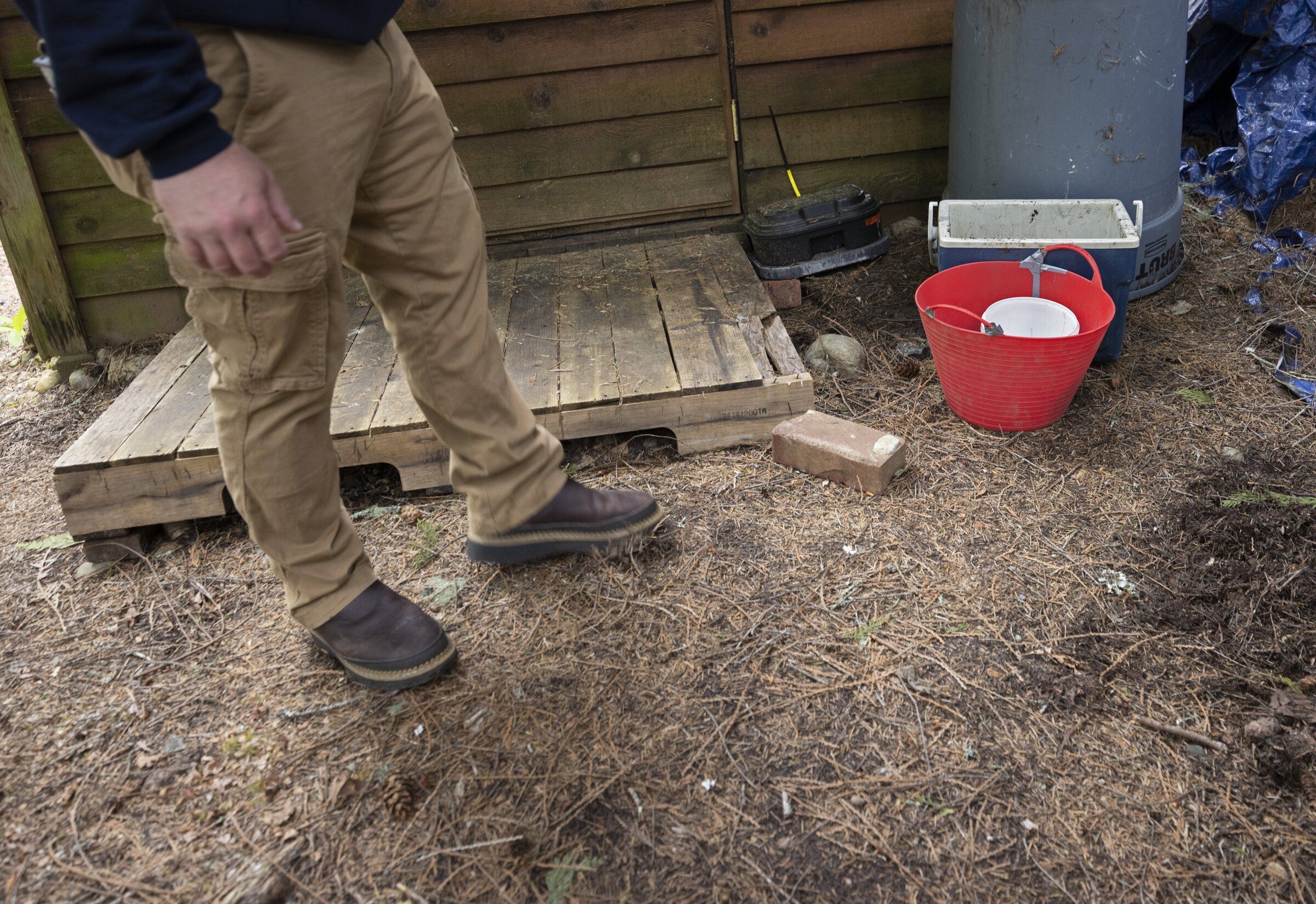 Jesse Duvall, a wildfire resilience coordinator for the Department of Natural Resouorces, kicks at branches and other debris lying in front of a little shed during a home assessment in Hoodsport, Mason County. (Ellen M. Banner / The Seattle Times, 2024)