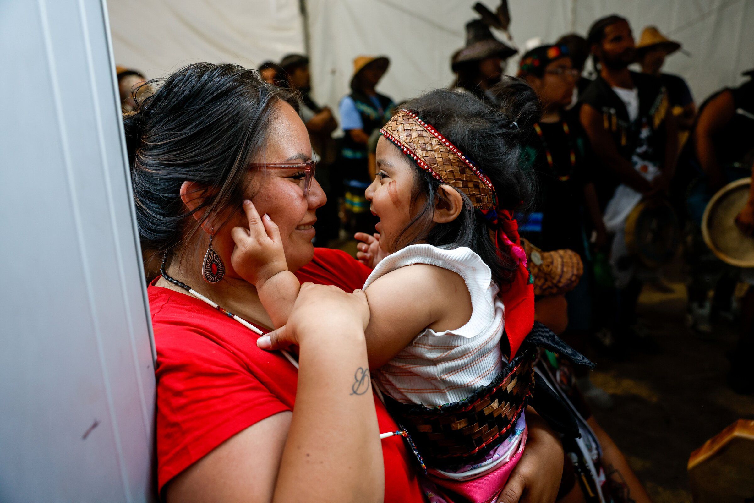 Lana Tsosi, an enrolled member of the Navajo Nation, holds 1-year-old Amethyst “GG” Jansen, an enrolled member of the Muckleshoot Tribe, before the Muckleshoot canoe family takes the ceremonial grounds for protocol during the 2026 Canoe Journey to Nisqually — Medicine Creek potlatch hosted by the Nisqually Tribe on Wednesday, Aug. 5. (Andrew Burk-Stephenson / The Seattle Times)