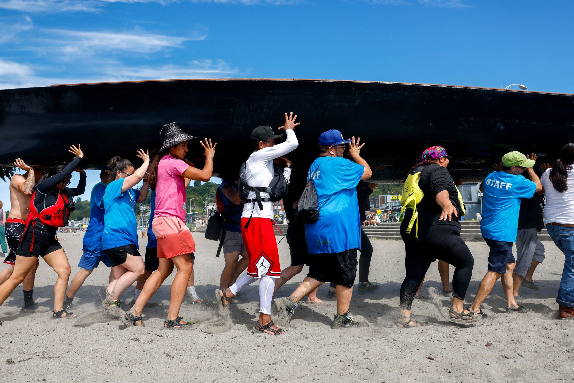 People, including the Muckleshoot Tribe’s canoe team, carry the canoe yəx̌ʷuləʔ səli (“Eagle Spirit”) on Alki Beach as canoes arrive and ask permission from their Muckleshoot hosts to come ashore in Seattle on Wednesday, July 29. (Andrew Burk-Stephenson / The Seattle Times)