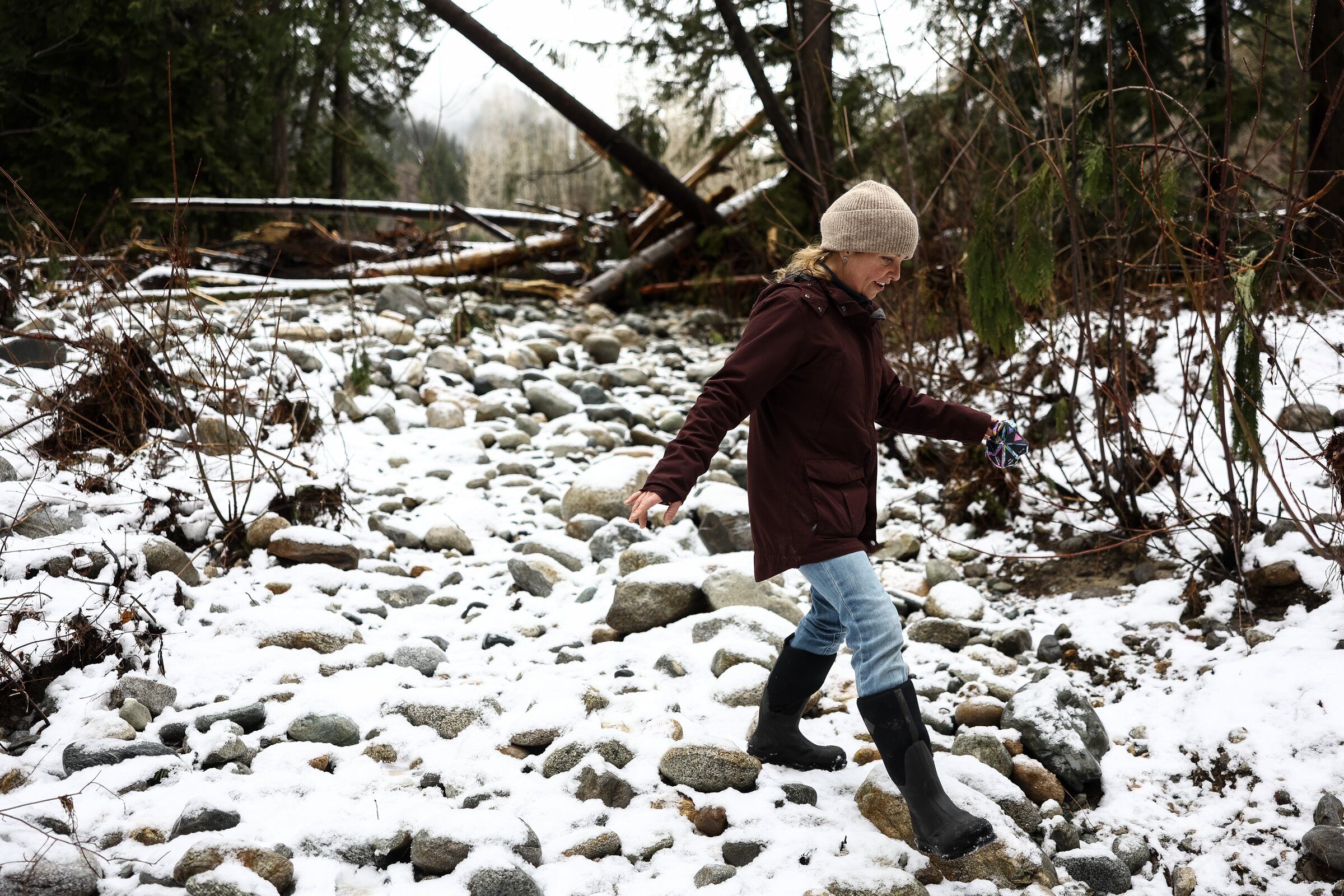 Mandy Kitchell treads carefully across rocks left by December flooding on Feb. 23, 2026, in Stehekin. Kitchell and at least a dozen other neighbors were waiting for an action plan by the National Park Service. (Nick Wagner / The Seattle Times)