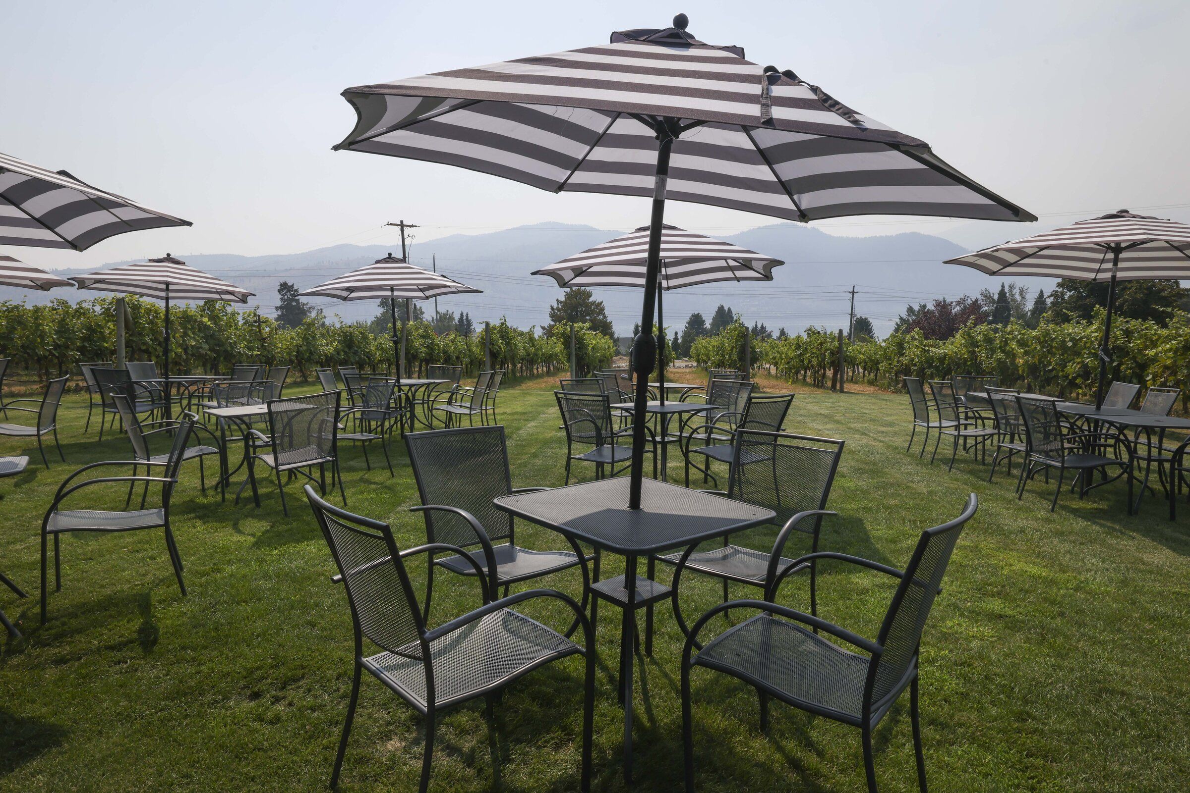 A few guests sit outside Succession Wines as wildfire smoke fills the sky in the distance; Manson, Thursday, Aug. 20. (Ivy Sebayo / The Seattle Times)